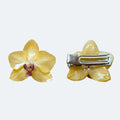 Pinza Orquídea amarilla preservada en resina, vista frontal y trasera sobre fondo claro, con cierre metálico plateado tipo cocodrilo.
