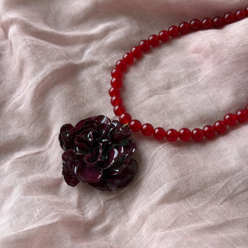 Collar Clavel Ingrid sobre tela rosa, clavel burdeos en cuentas rojas vista superior