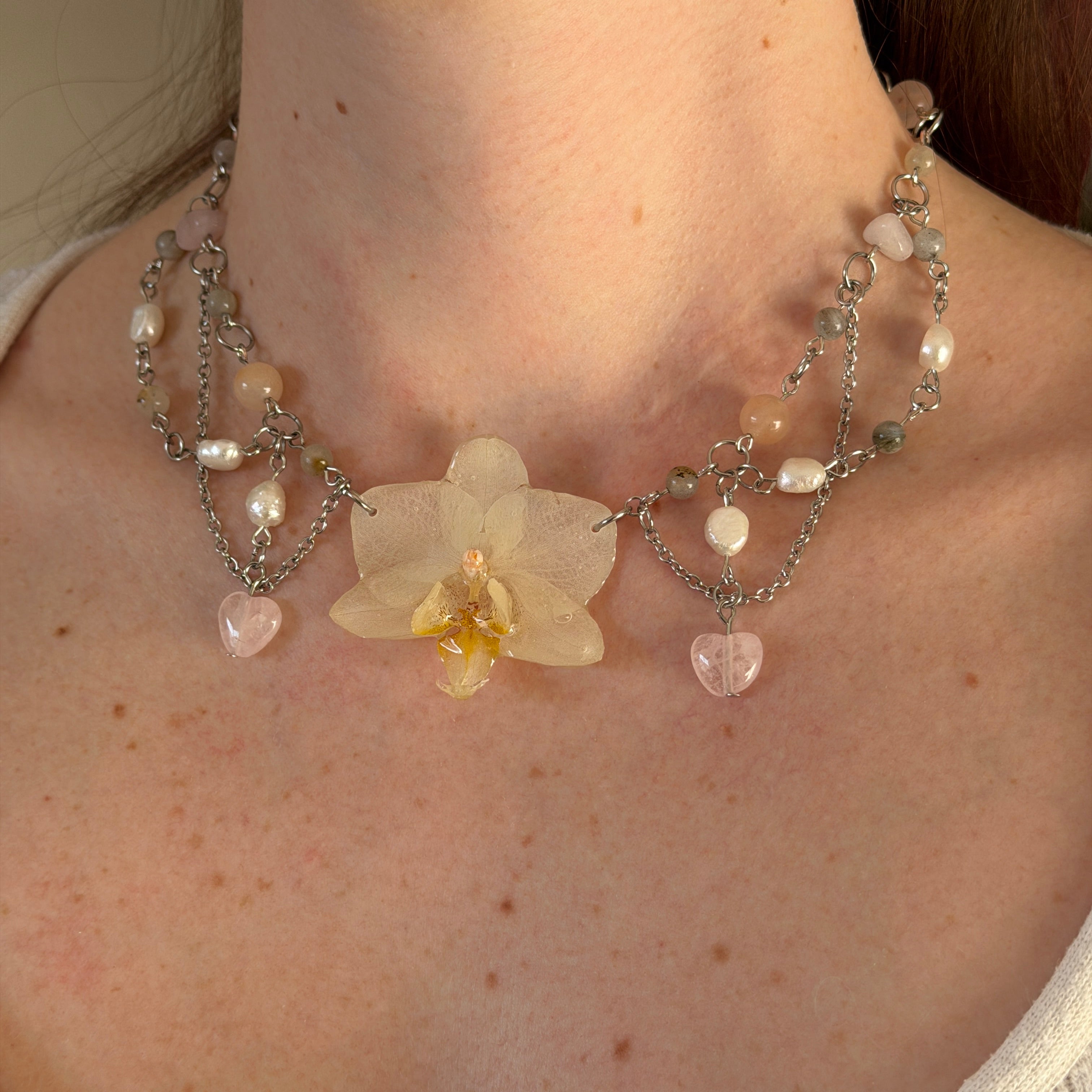 Modelo luciendo el Set Orquídea Niebla, collar con orquídea blanca en cadenas plateadas con corazones de cuarzo rosa