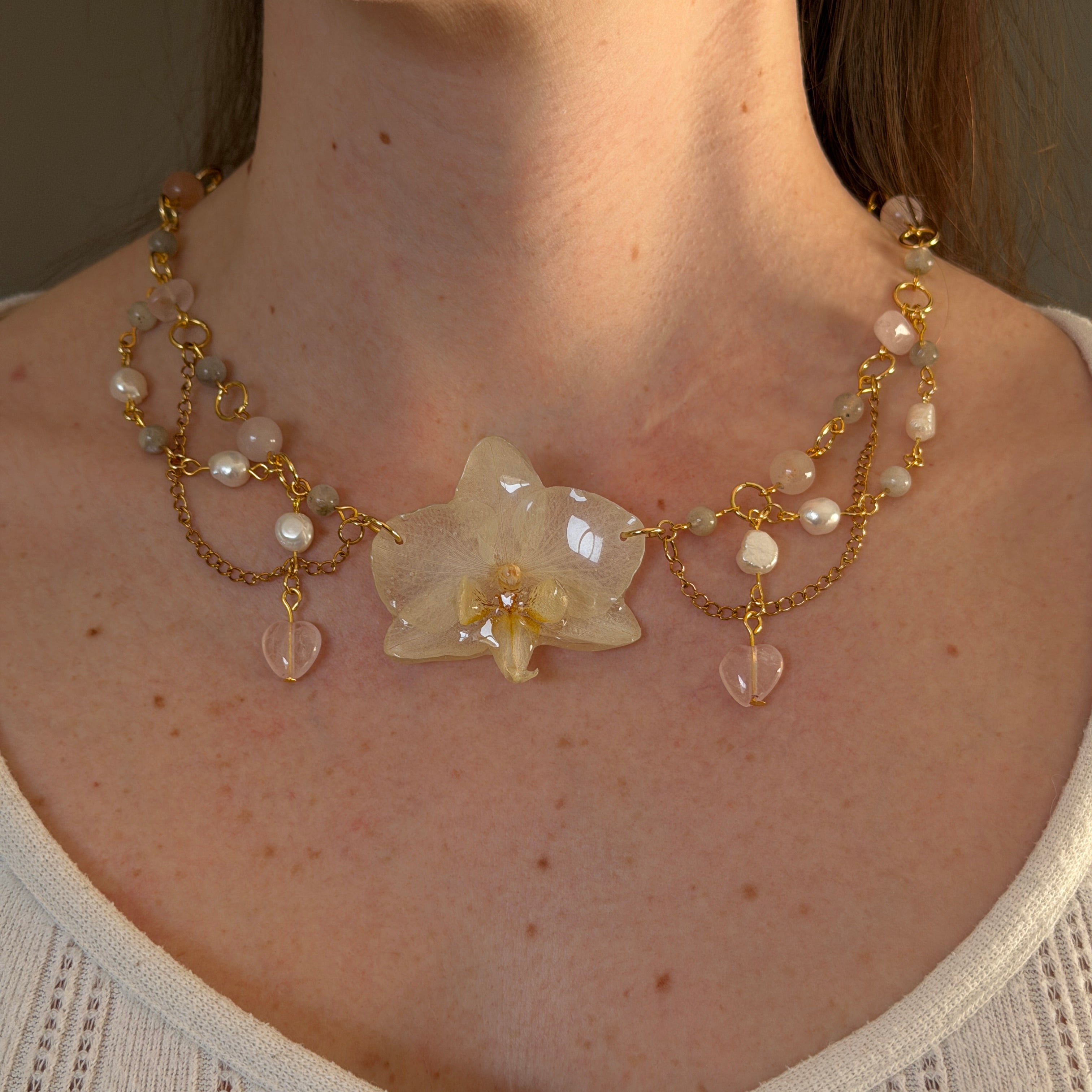 Set Orquídea Estela de Aurum Orchid con collar de orquídea blanca preservada en resina, cadena dorada con perlas naturales, cuarzo rosa y corazones colgantes, puesto sobre piel