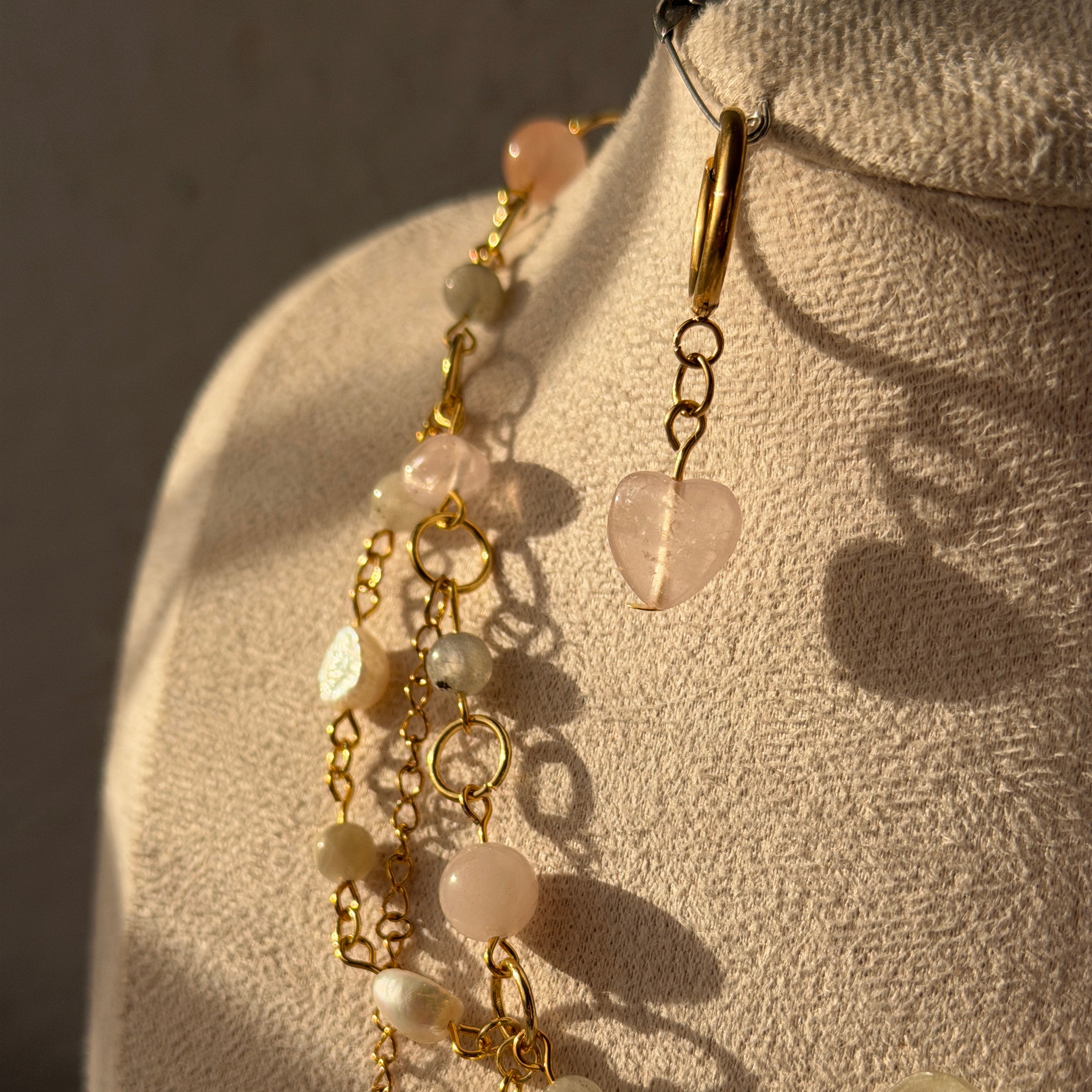 Detalle de la cadena del collar Orquídea Estela con perlas naturales, piedras de cristal, cuarzo rosa y cierre reasa dorado junto a los pendientes huggie con cuarzo rosa