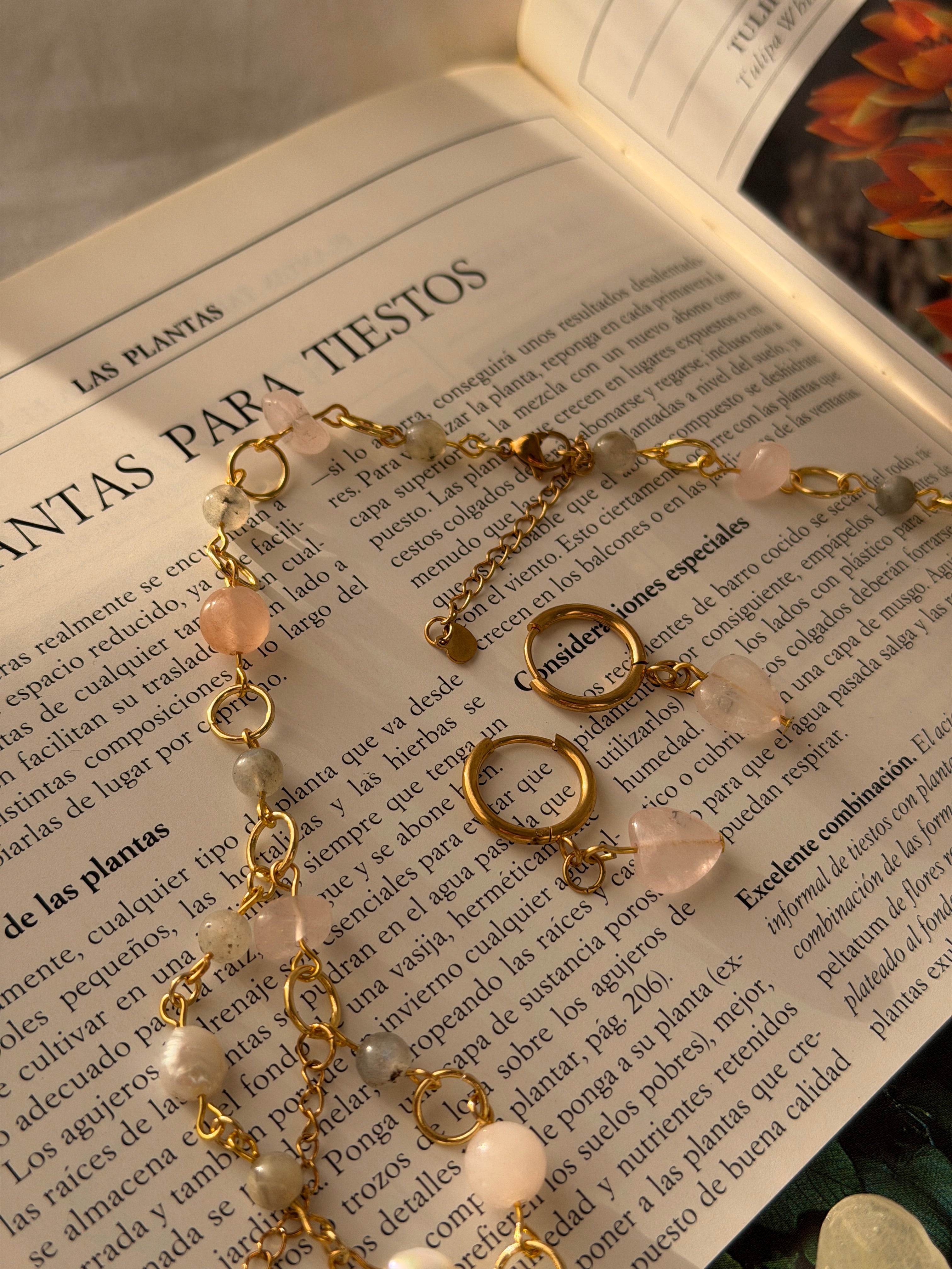 Set Orquídea Estela completo en flat lay sobre libro vintage: collar con orquídea phalaenopsis preservada en resina, cadena de perlas naturales y cuarzo rosa con pendientes huggie dorados