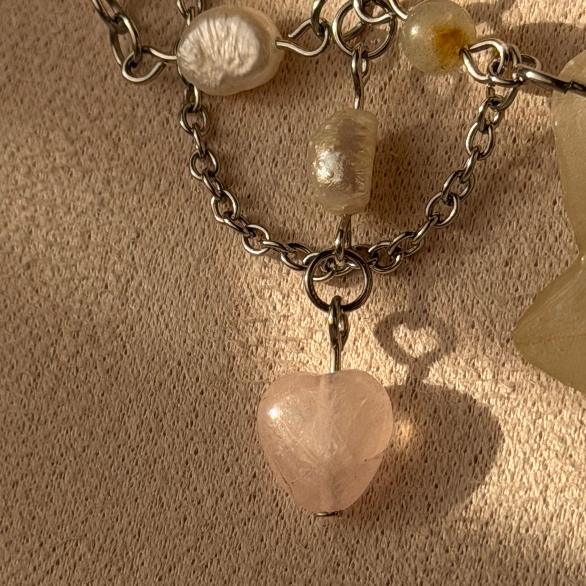 Detalle del colgante corazón de cuarzo rosa con cadena plateada y perlas del Set Orquídea Niebla