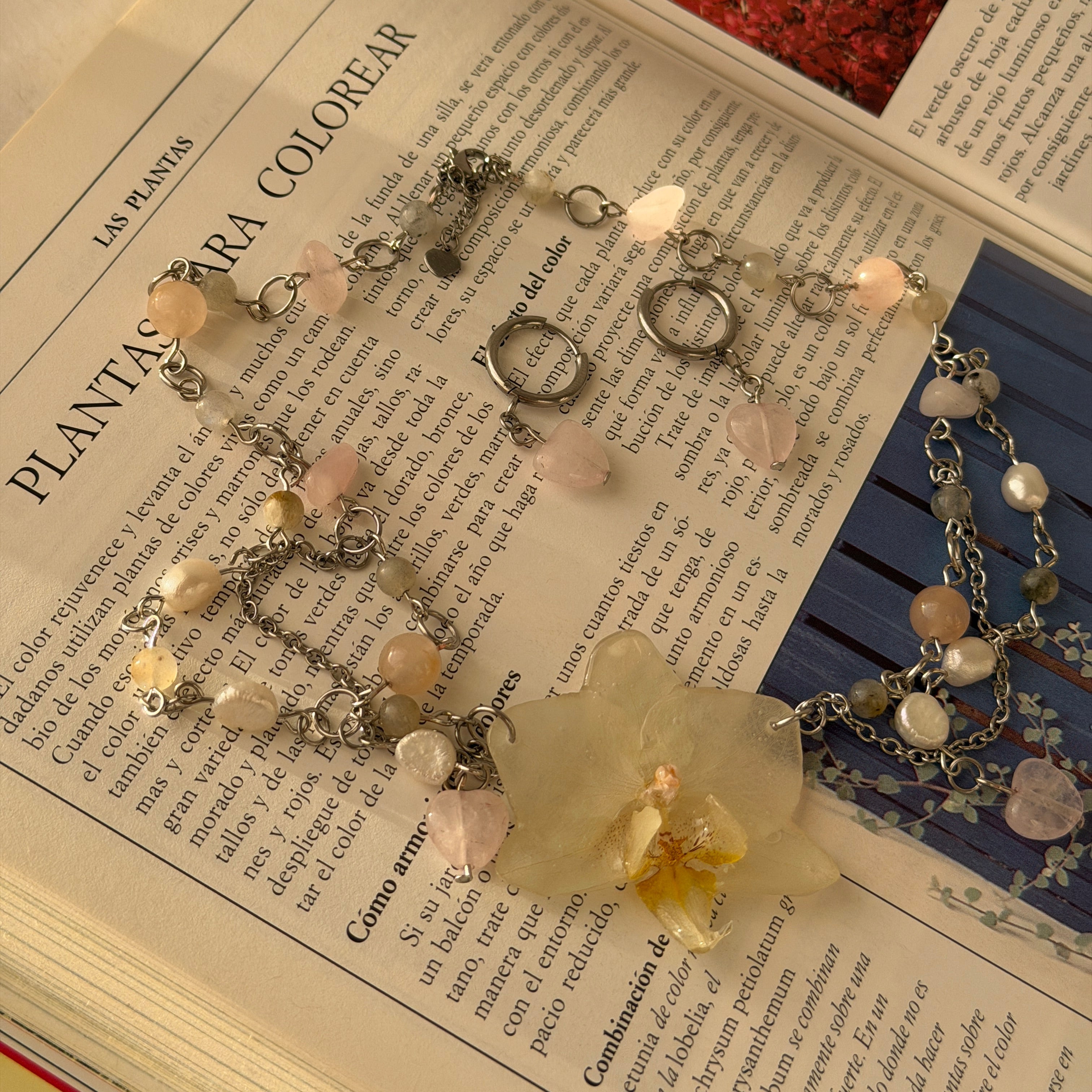 Set Orquídea Niebla extendido sobre libro, collar con orquídea blanca, cuentas de cuarzo rosa y perlas naturales