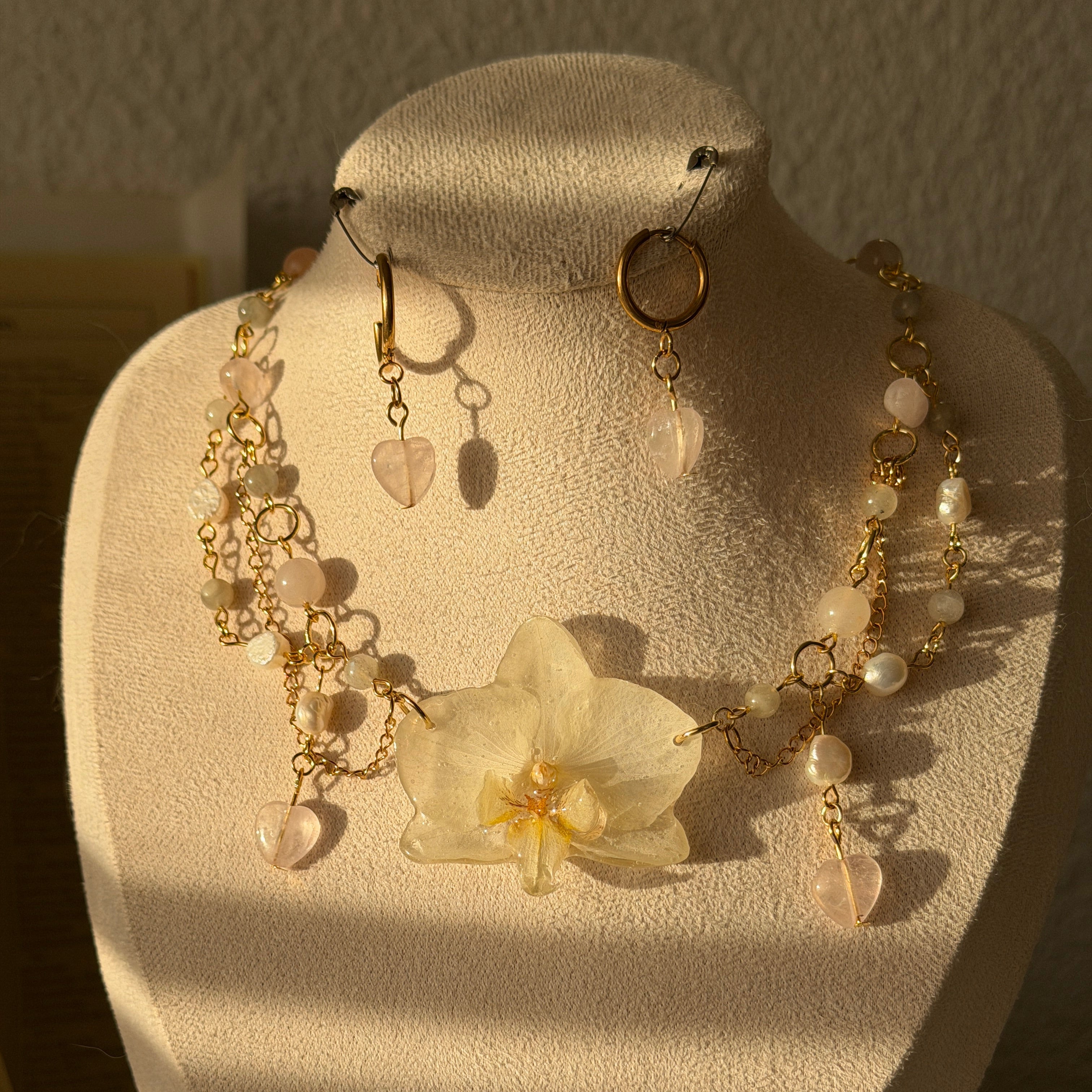 Detalle lateral del collar Orquídea Estela mostrando las perlas naturales, piedras de cristal, cuarzo rosa y cadenitas doradas colgantes con corazón de cuarzo rosa