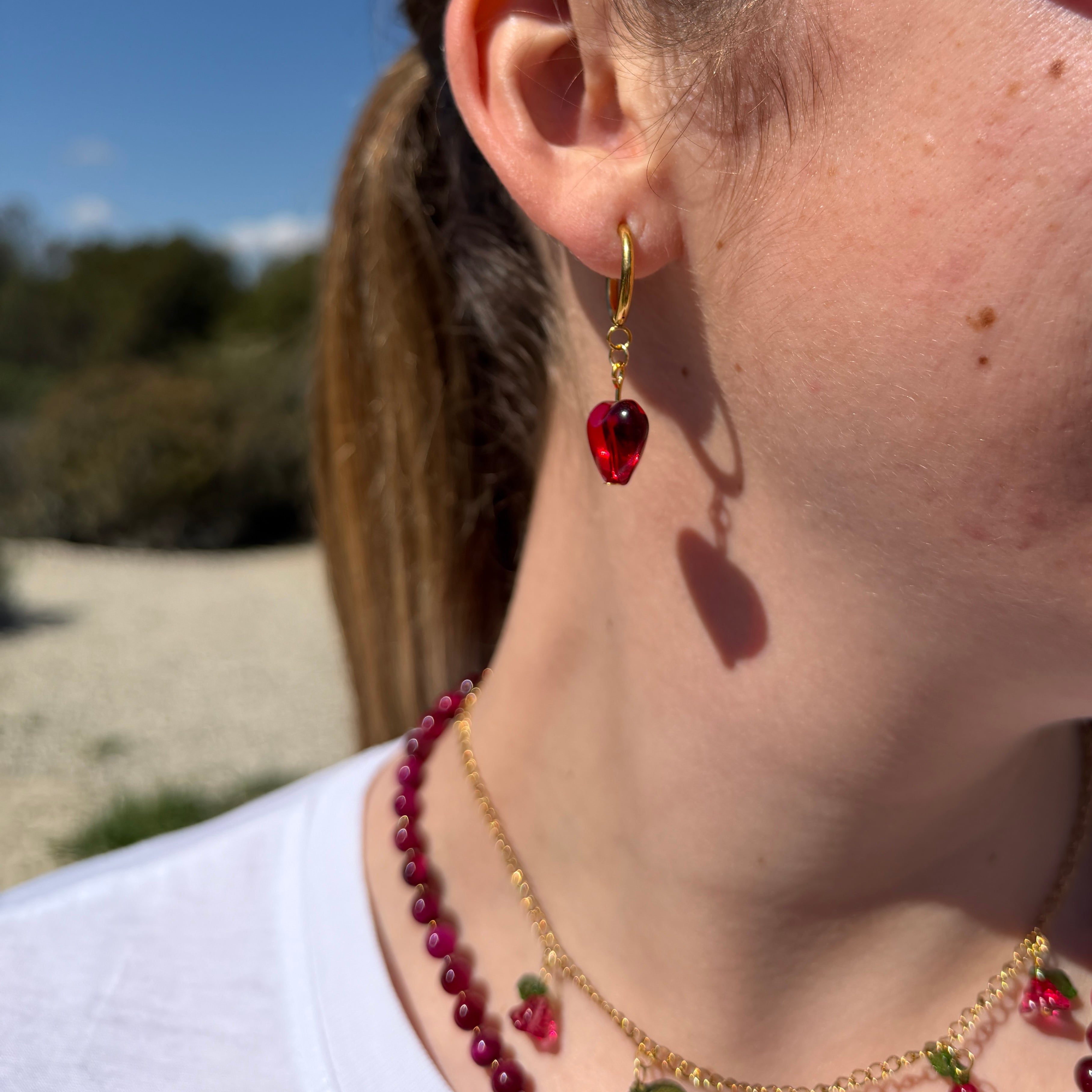 Detalle del pendiente del Set Margarita Cereza: aro dorado con corazón de cristal rojo en oreja