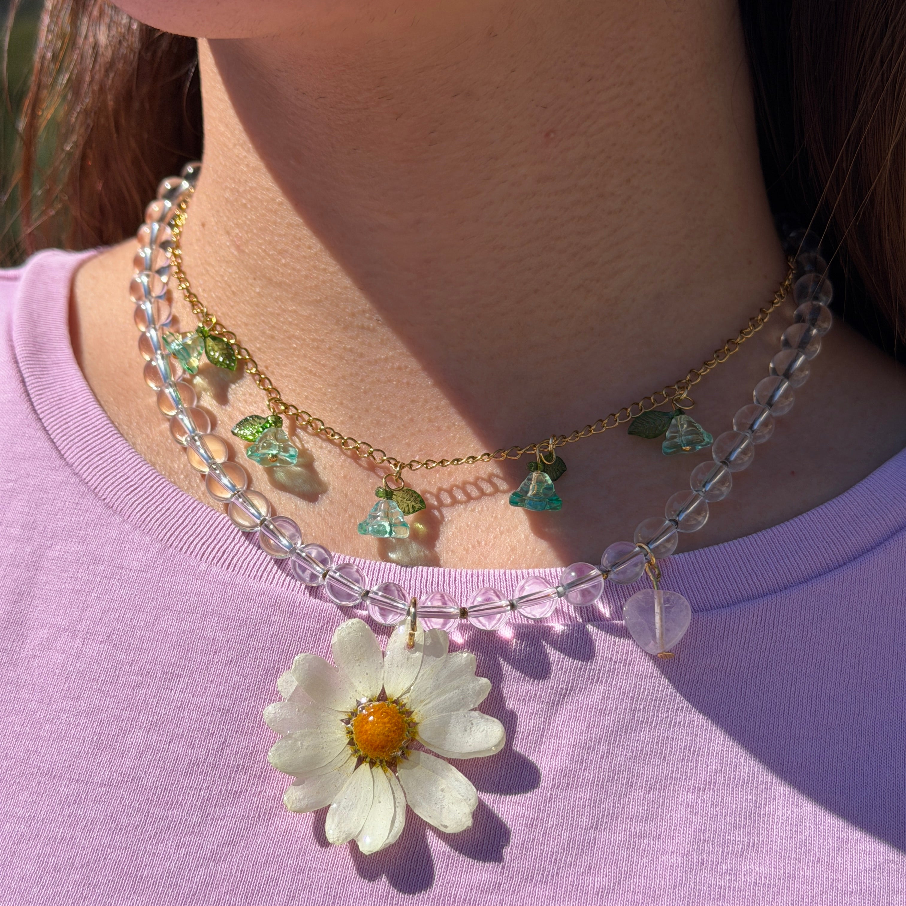 Set Margarita Brisa puesto mostrando la margarita preservada en resina como colgante central, cadena doble con piedras transparentes y flores de acrílico verdes y turquesa con corazón de cuarzo rosa