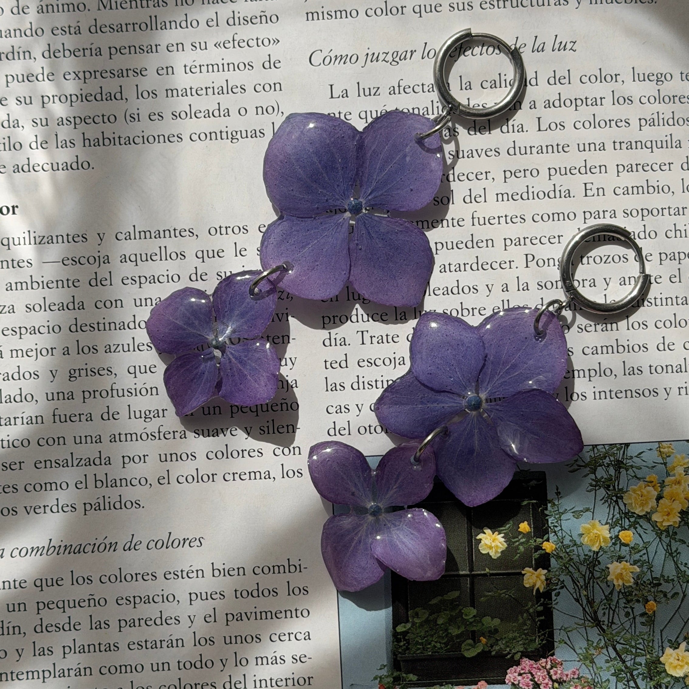 Par de Pendientes Hortensia Dúo con dos flores lavanda en aro plateado sobre libro con jardín