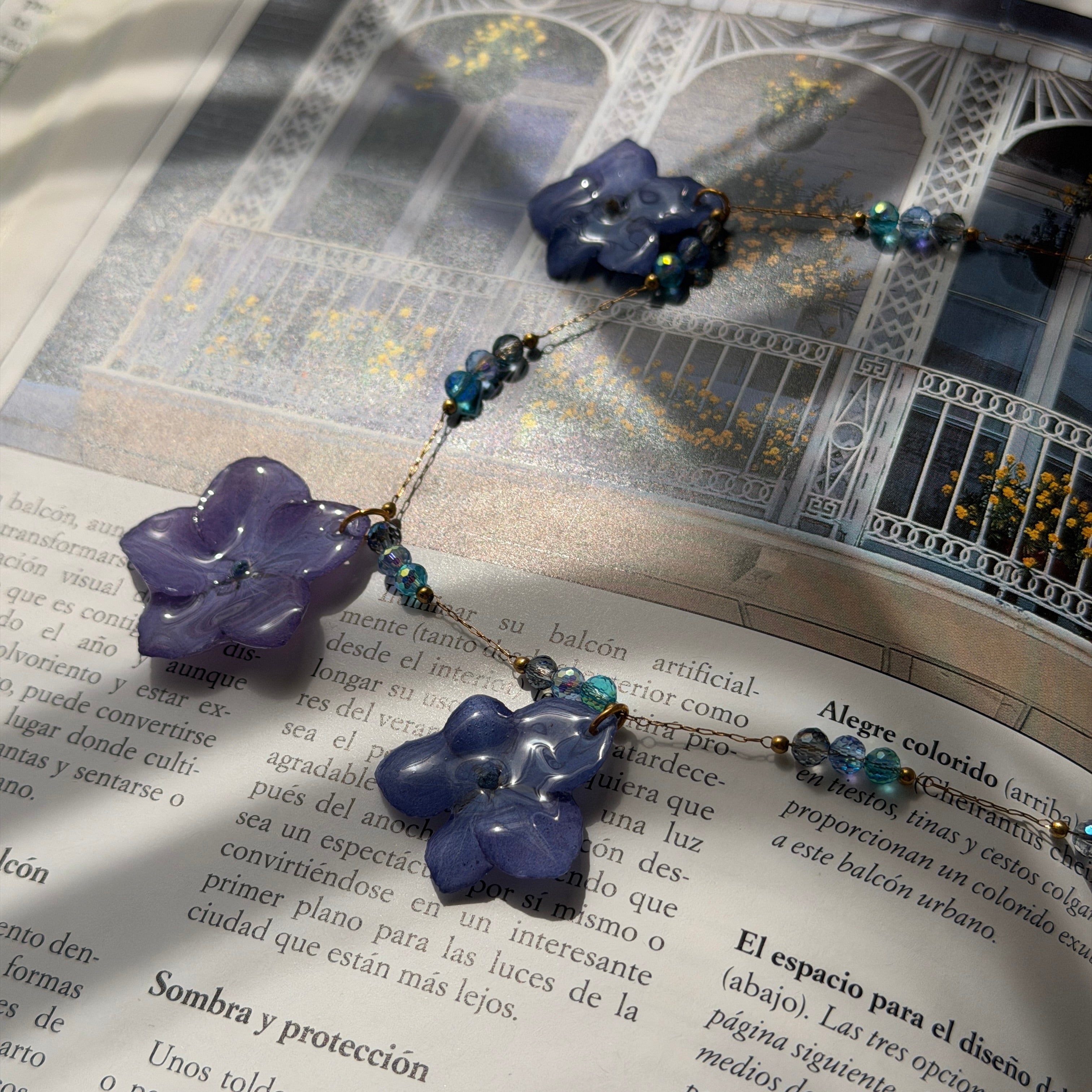 Collar Hortensia Celeste con hortensias lavanda y cuentas de cristal azul sobre libro abierto
