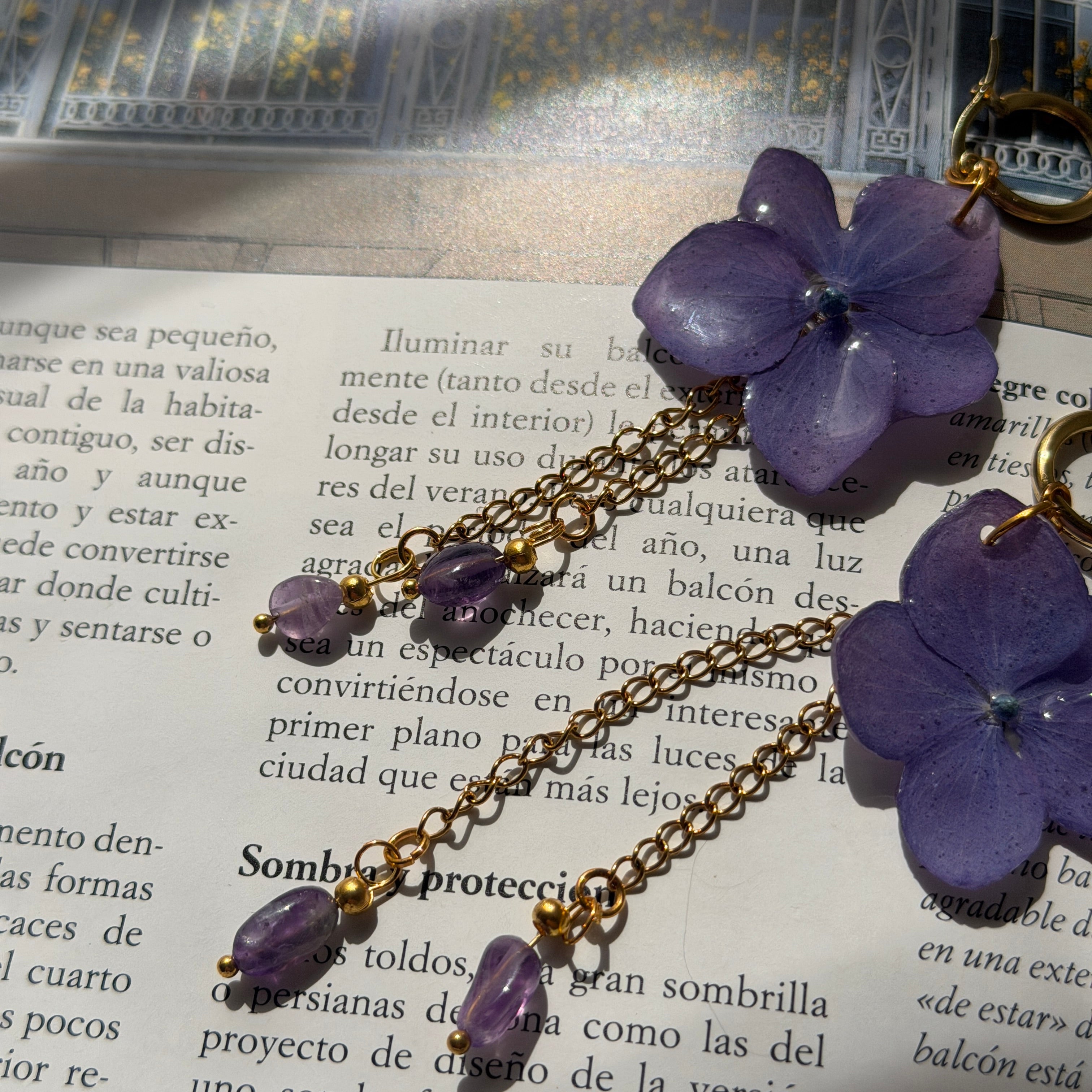 Par de Pendientes Hortensia Cascada sobre libro: flores lavanda con cadenas doradas y amatistas