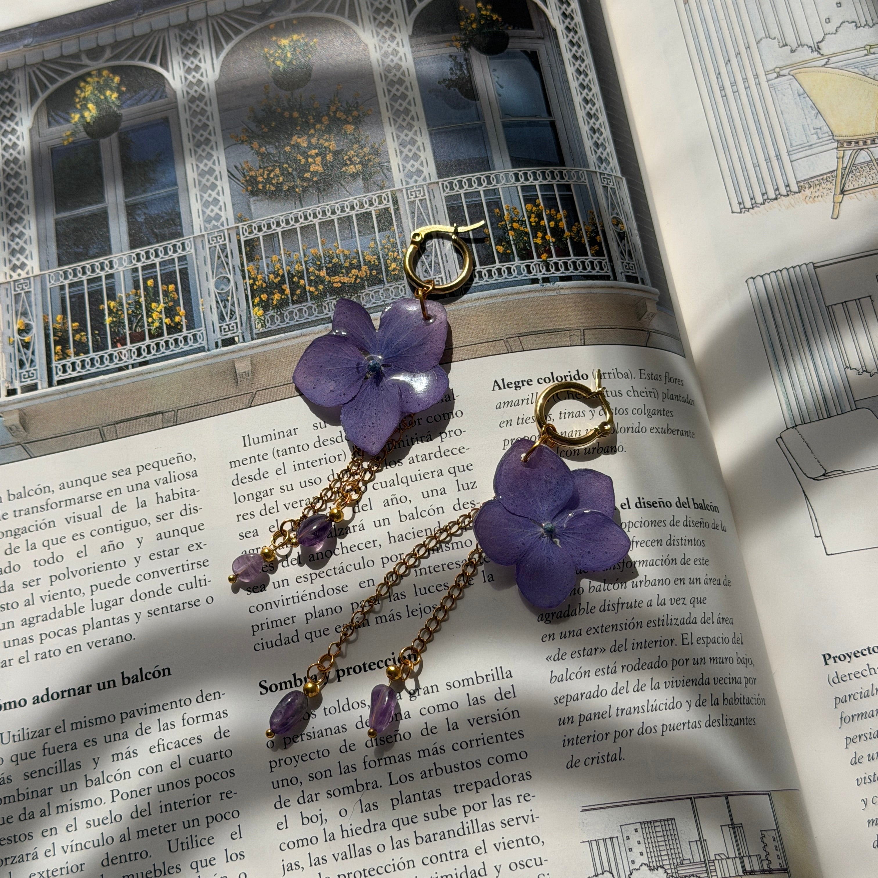 Pendientes Hortensia Cascada sobre libro con balcón: flores lavanda, cadenas doradas y amatistas