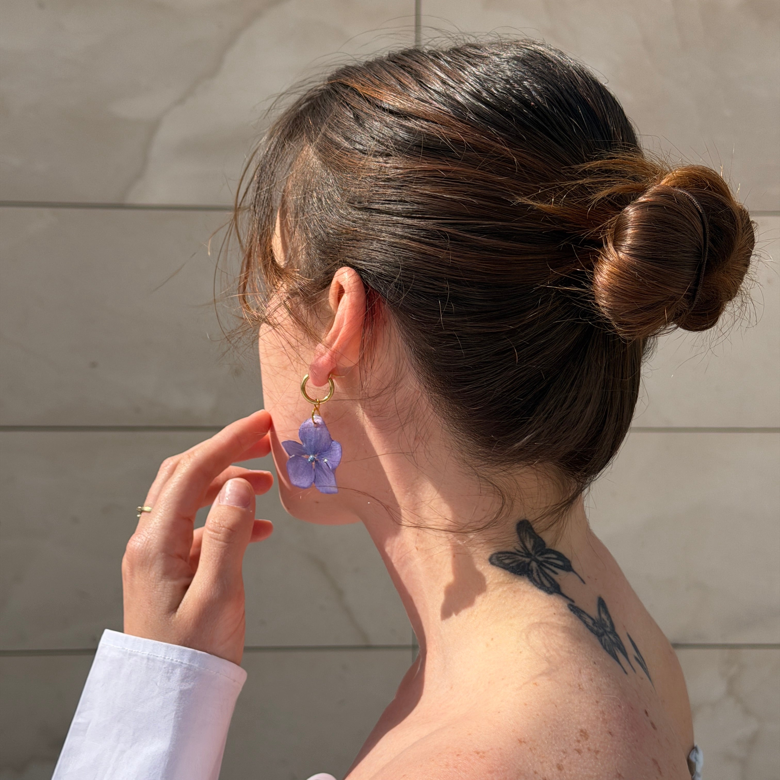 Par de pendientes de hortensia lavanda con aros dorados sobre libro abierto con jardín al fondo
