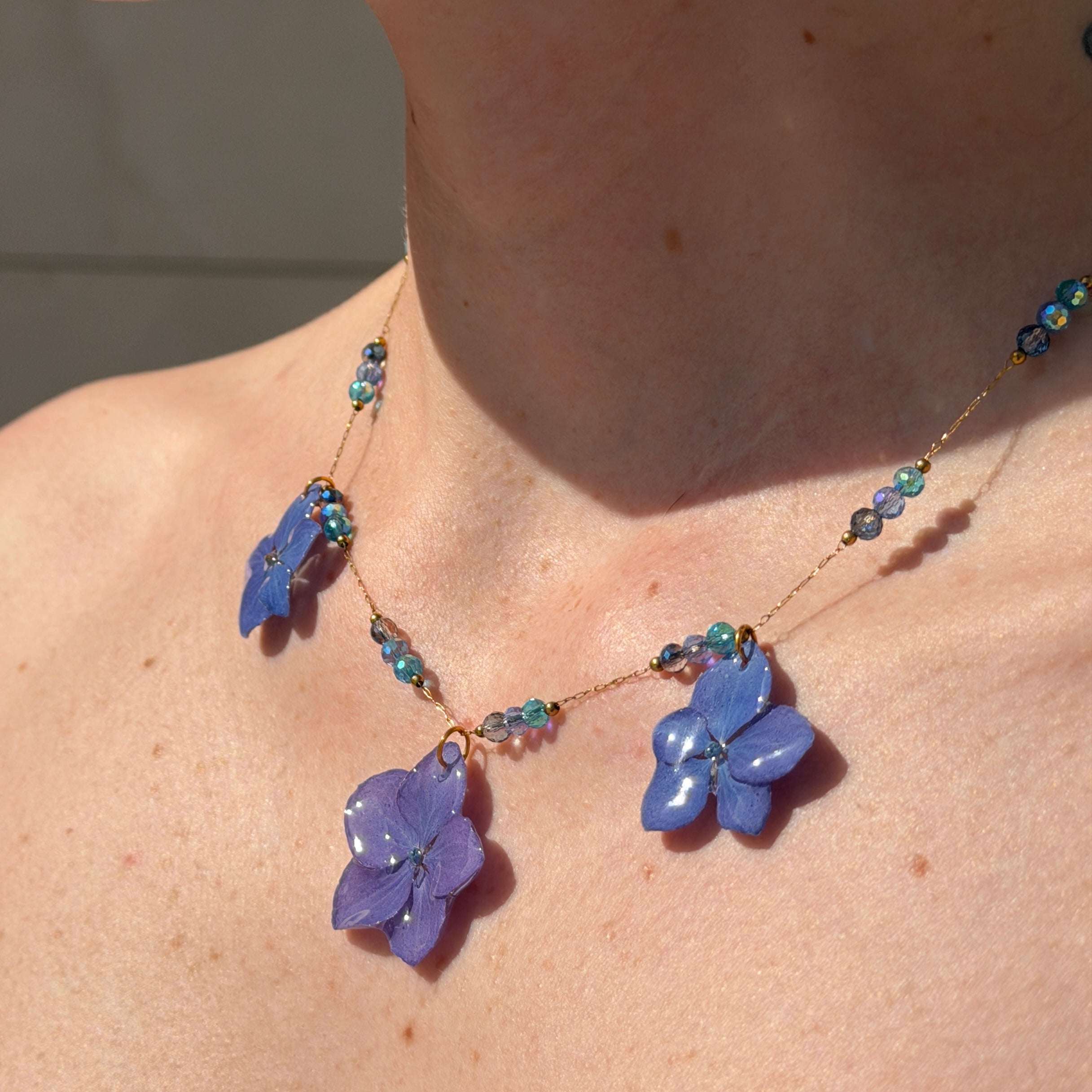 Collar de tres hortensias lavanda con cuentas de cristal azul sobre libro abierto, vista lateral