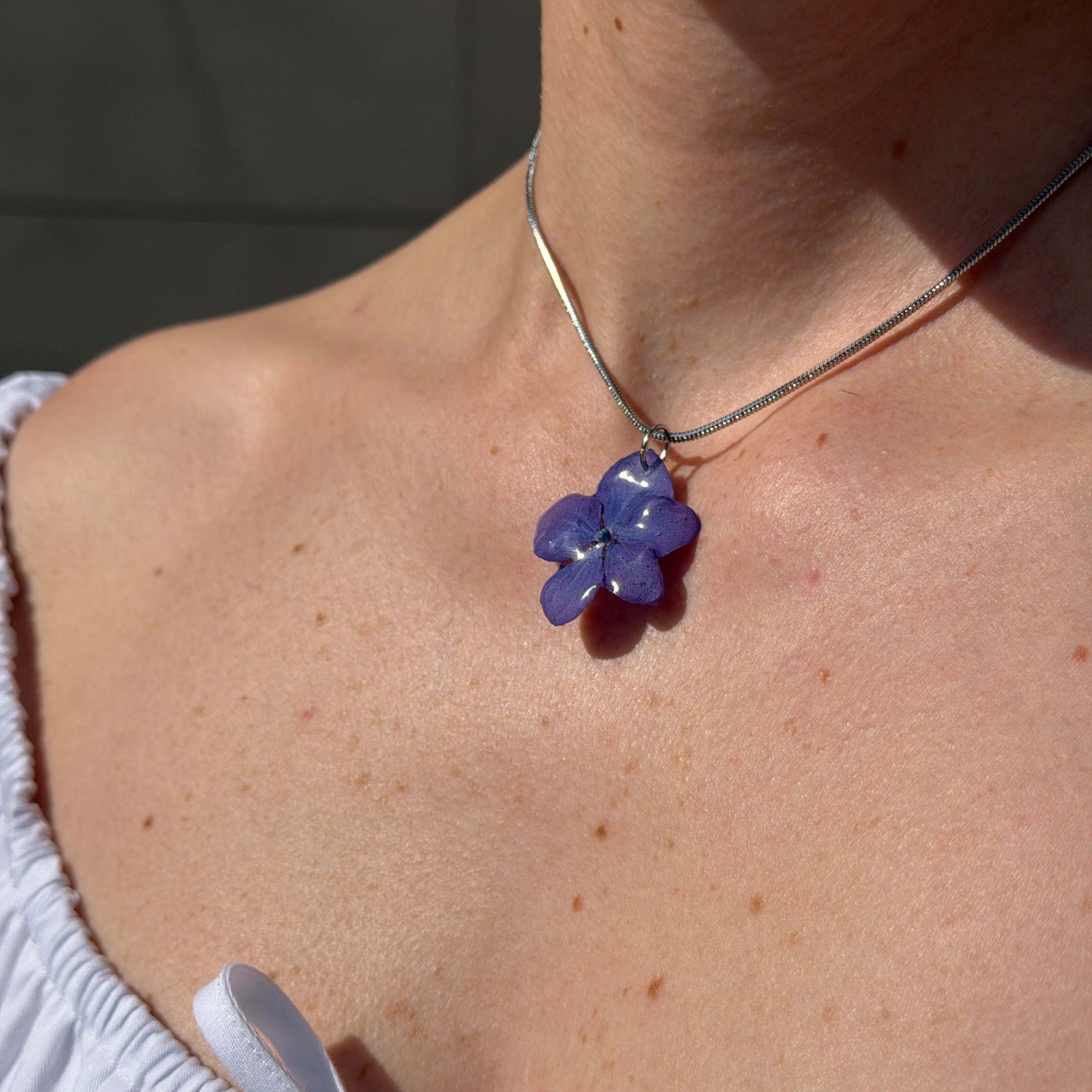 Modelo con collar de hortensia lavanda en resina y cadena plateada, cuello al sol, vista lateral