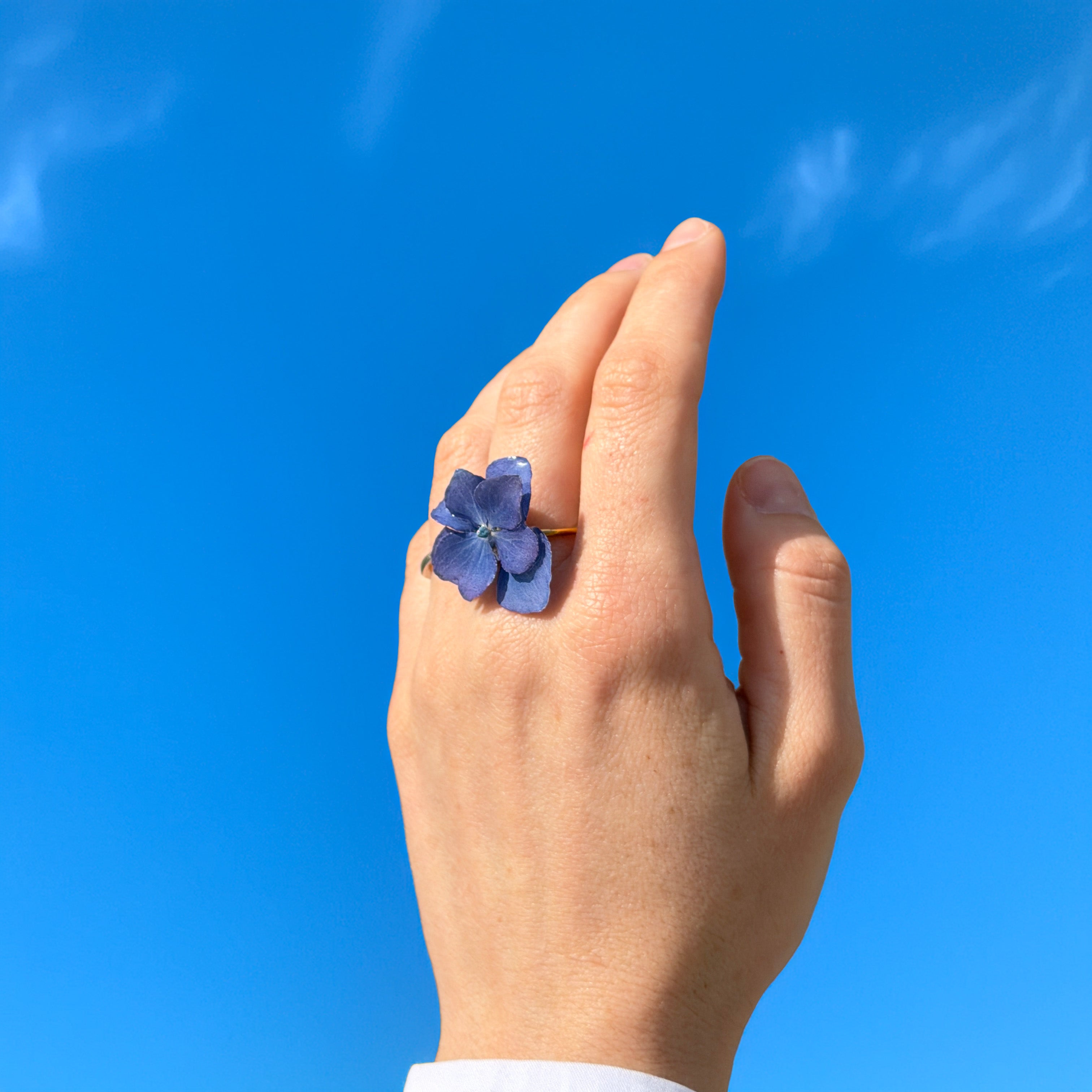 Anillo de hortensia lavanda en resina lucido por modelo elevando la mano hacia el cielo azul
