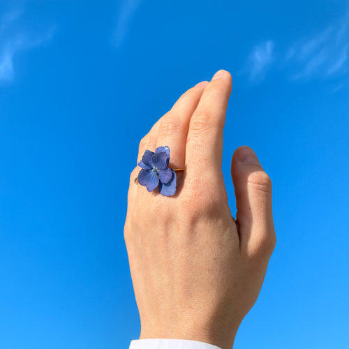 Anillo de hortensia lavanda en resina lucido por modelo elevando la mano hacia el cielo azul
