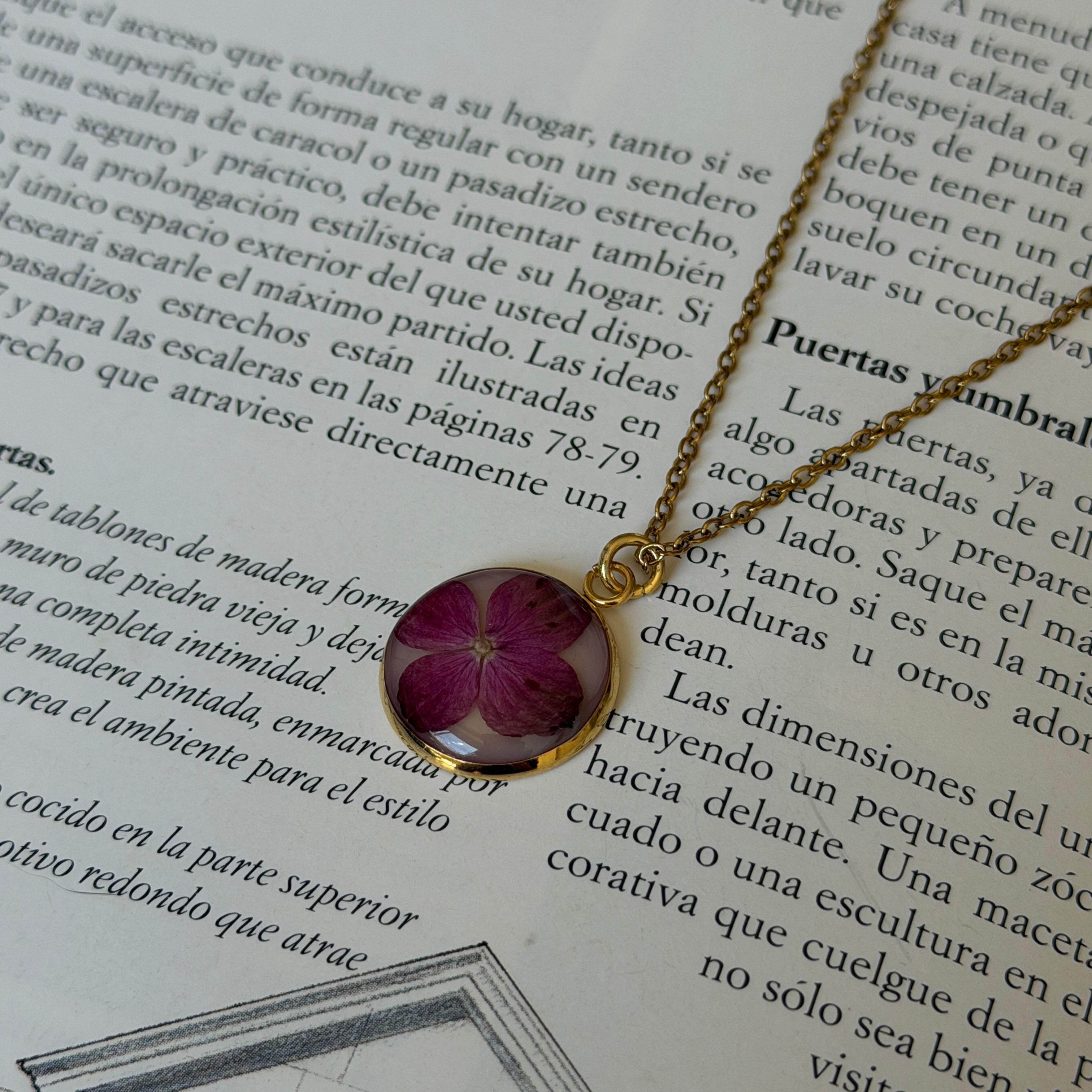 Collar Hortensia Mireia sobre libro abierto, medallón dorado redondo con hortensia fucsia y cadena