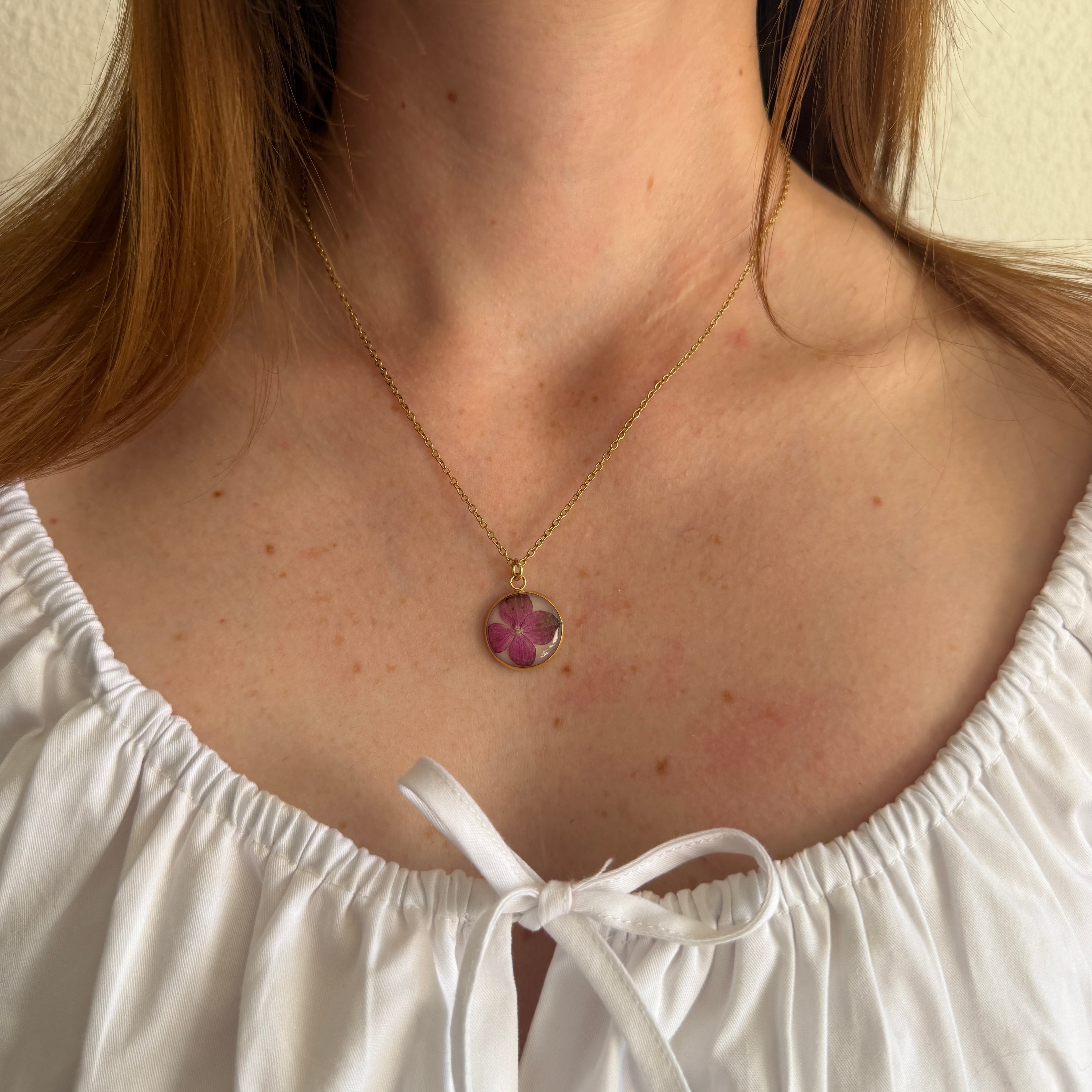 Modelo con Collar Hortensia Mireia, medallón dorado con hortensia fucsia, top blanco de tirantes