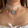 Modelo con Gargantilla Leticia: encaje blanco con medallón oval plateado, hortensia azul y perlas