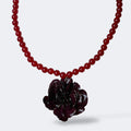 Collar colgante con clavel burdeos oscuro preservado en resina sobre hilo de cuentas rojas, fondo blanco