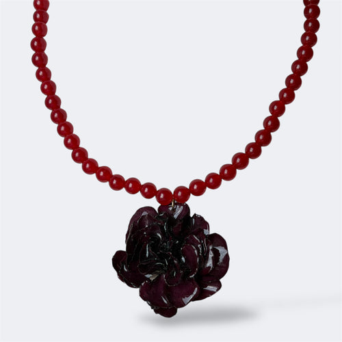 Collar colgante con clavel burdeos oscuro preservado en resina sobre hilo de cuentas rojas, fondo blanco