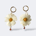 Par de pendientes de margarita blanca con cristal gota ámbar en aros dorados, fondo gris