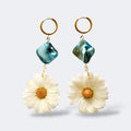 Par de pendientes de margarita blanca con cuenta nacar azul océano en aros dorados, fondo gris