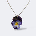 Collar colgante de pensamiento natural preservado en resina violeta y azul profundo, cadena plateada, fondo blanco