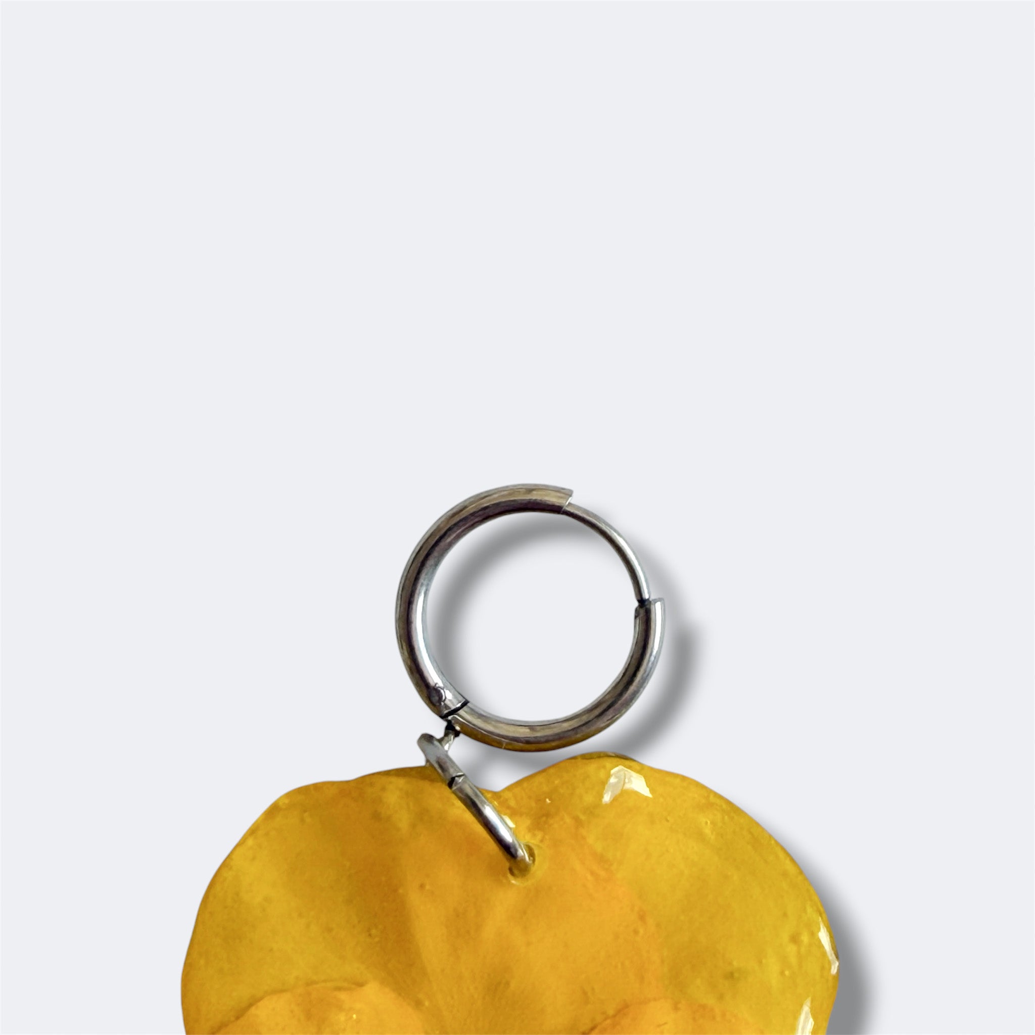 Detalle del aro plateado con pensamiento candela amarillo preservado, fondo gris liso