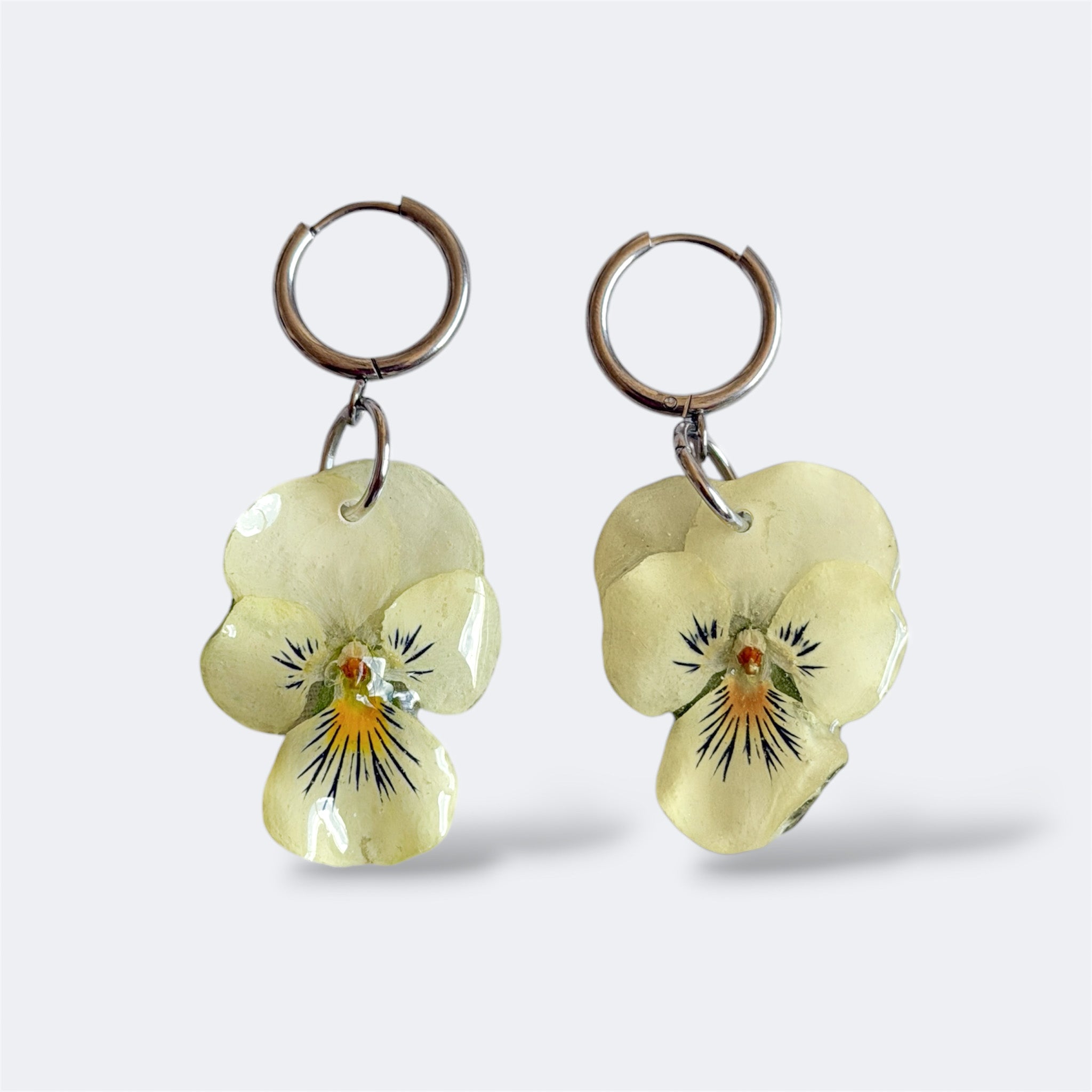 Par de Pendientes Pensamiento Vainilla con flor crema-amarillo pálido en aros plateados, fondo gris