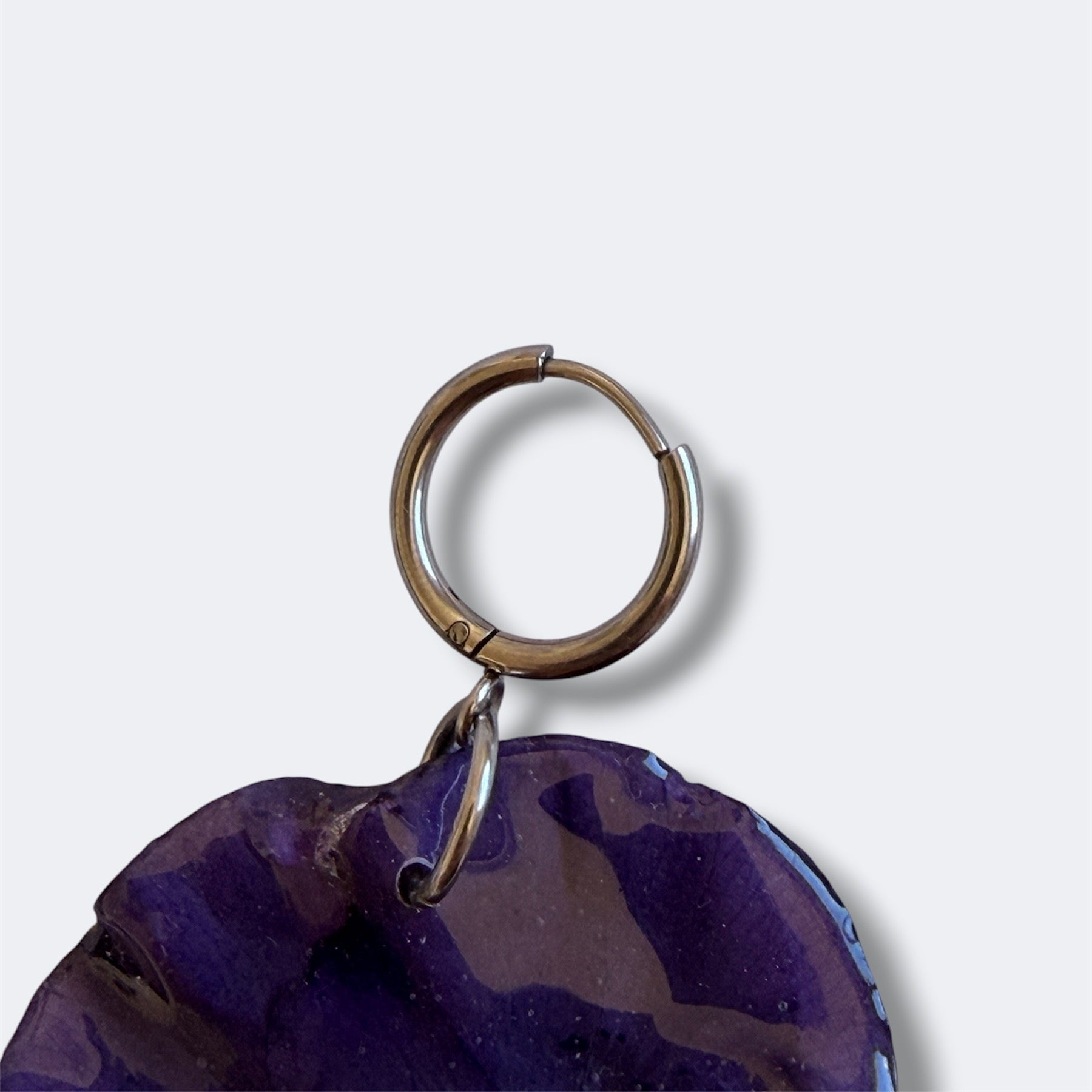 Detalle del aro plateado con pensamiento violeta preservado, fondo gris liso