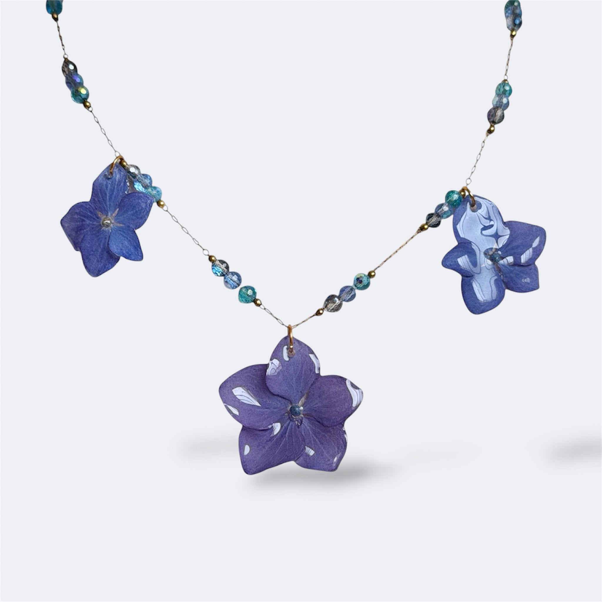Collar con tres hortensias azul lavanda en resina y cuentas de cristal azul en cadena dorada fina