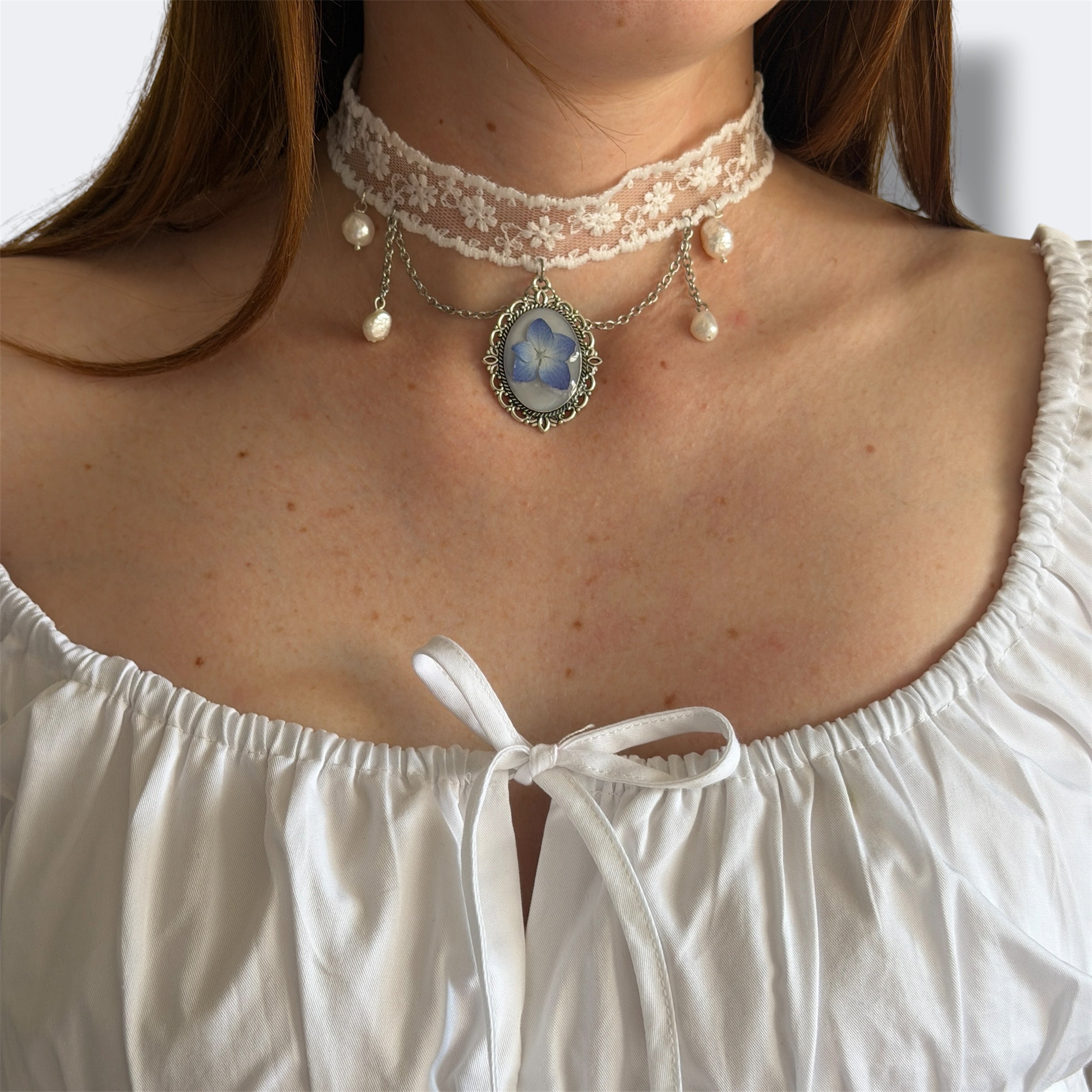 Modelo con Gargantilla Leticia de perfil: encaje blanco con hortensia azul en medallón y perlas