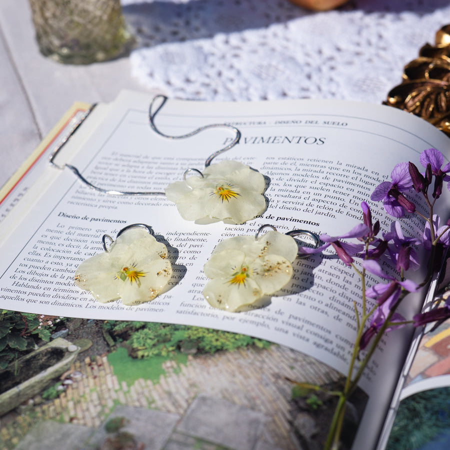 Collar y pendientes Pensamiento Alborada en flatlay sobre libro con mantel de encaje y flores lilas