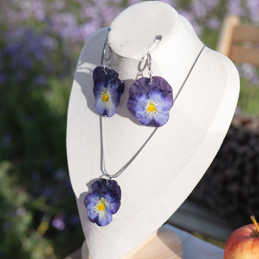 Mujer con collar y pendientes de pensamiento violeta en campo de flores moradas con pañuelo rojo
