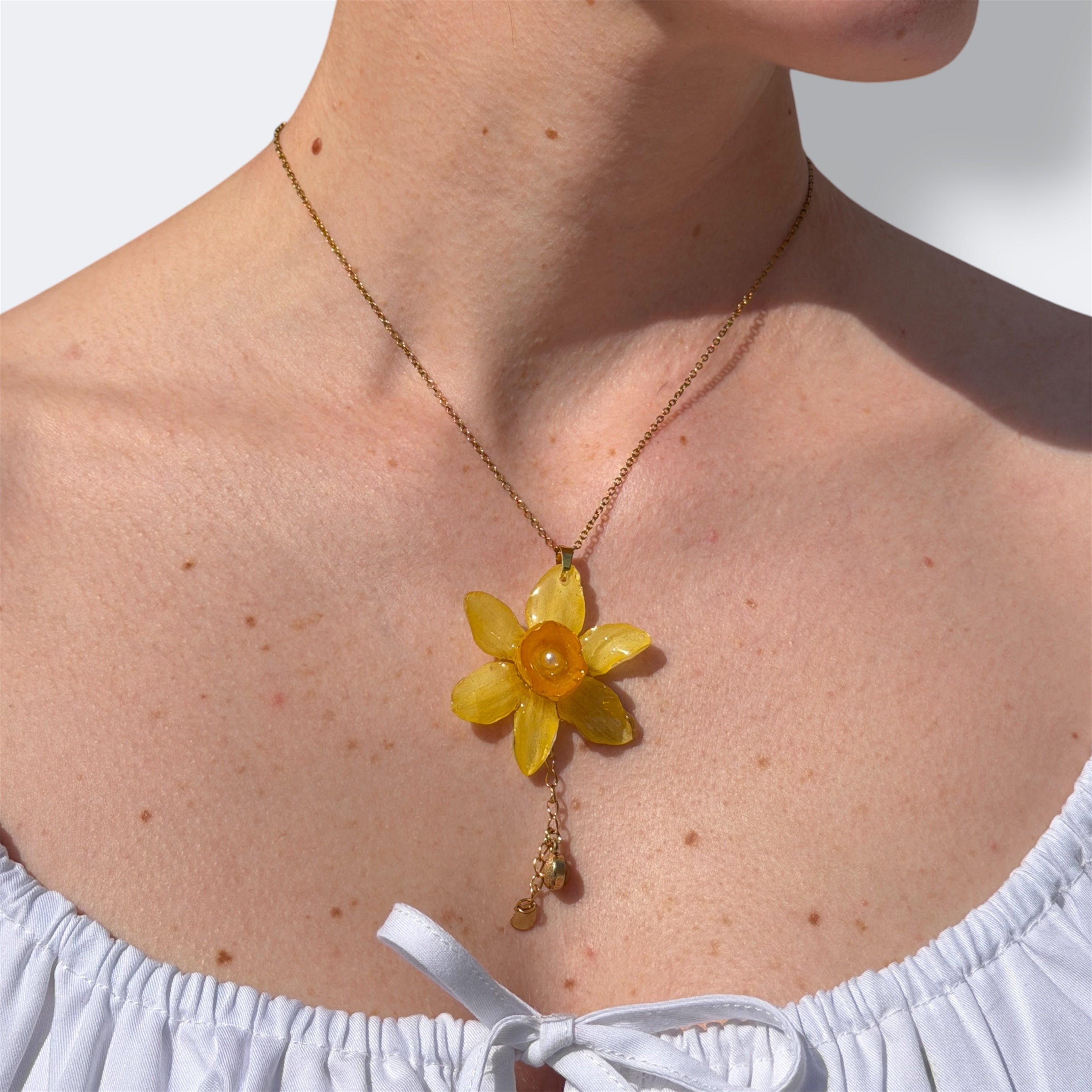 Detalle de mujer llevando collar de narciso amarillo encapsulado en resina sobre el pecho