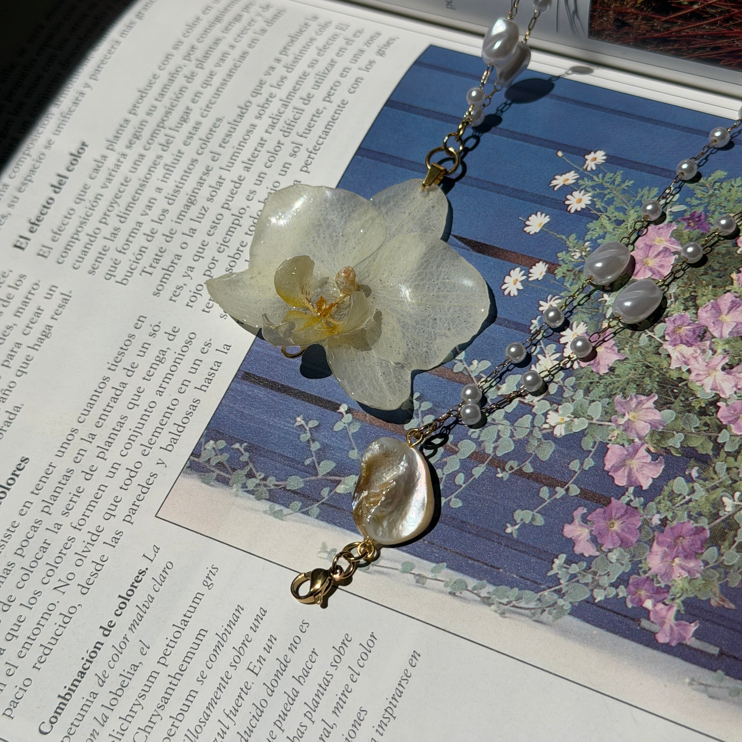 Detalle de orquidea marfil encapsulada en resina sobre blusa blanca, con cadena de perlas