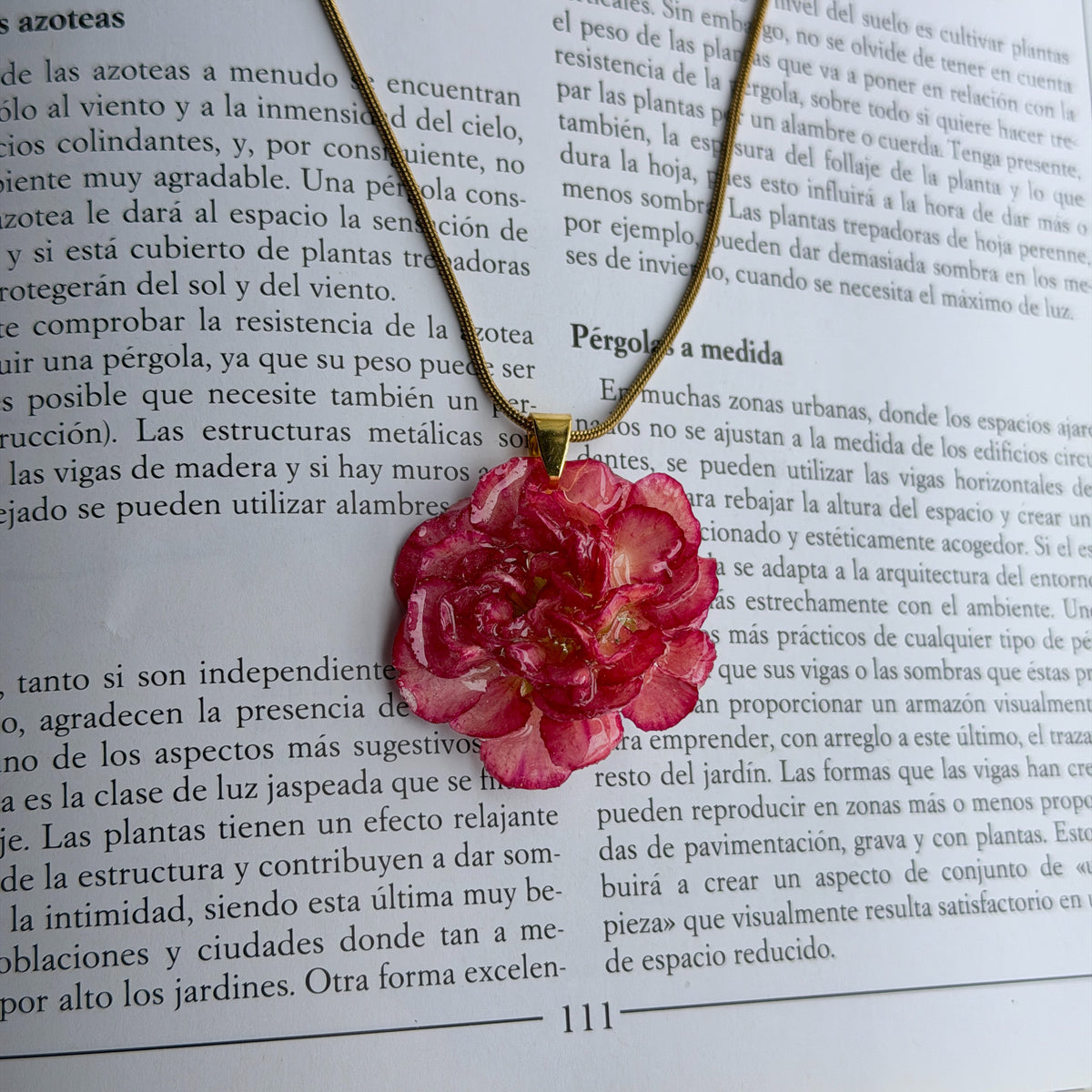 Collar Clavel Júpiter, clavel fucsia encapsulado en resina, sobre las páginas abiertas de un libro de jardinería
