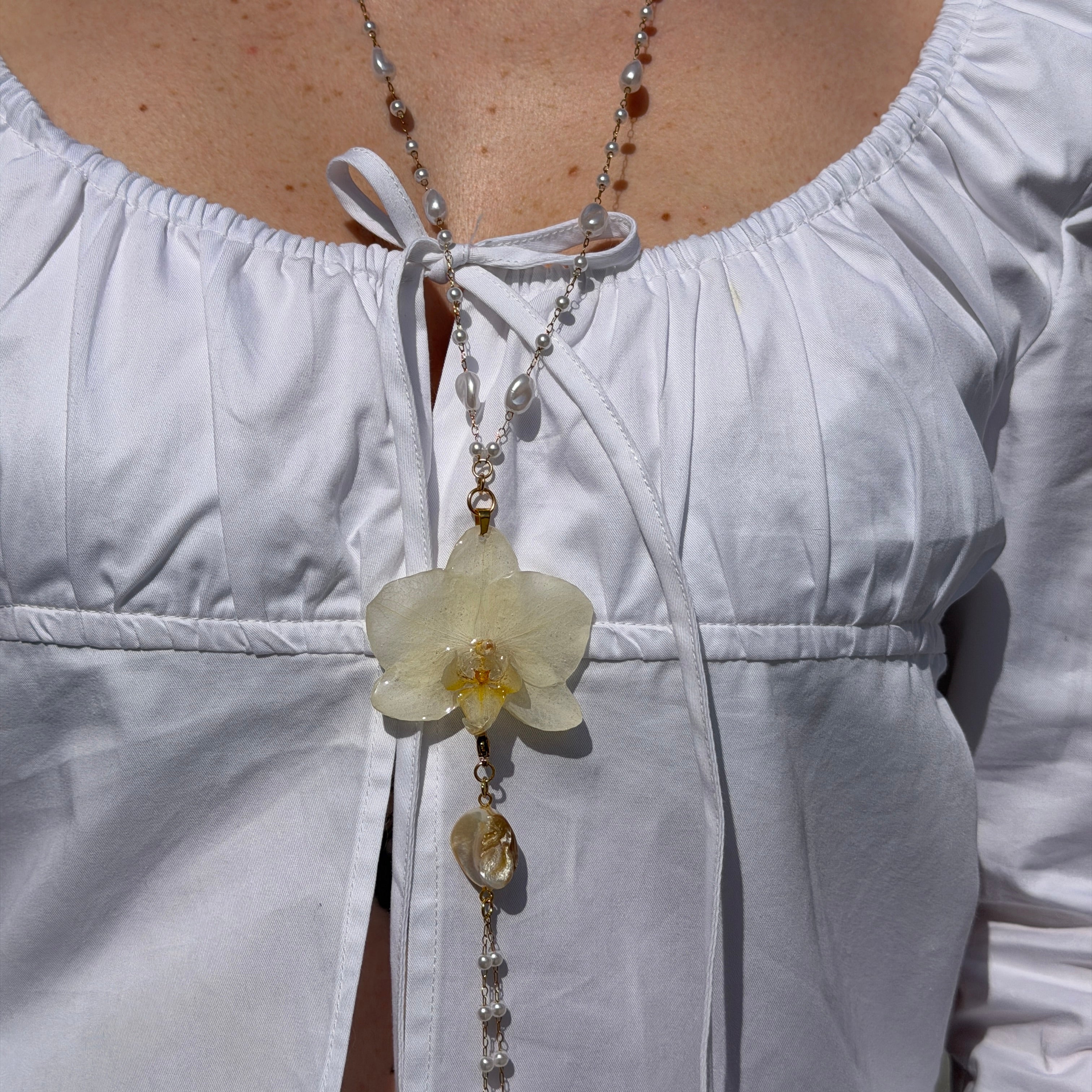Mujer llevando collar largo de orquidea marfil encapsulada en resina sobre el escote