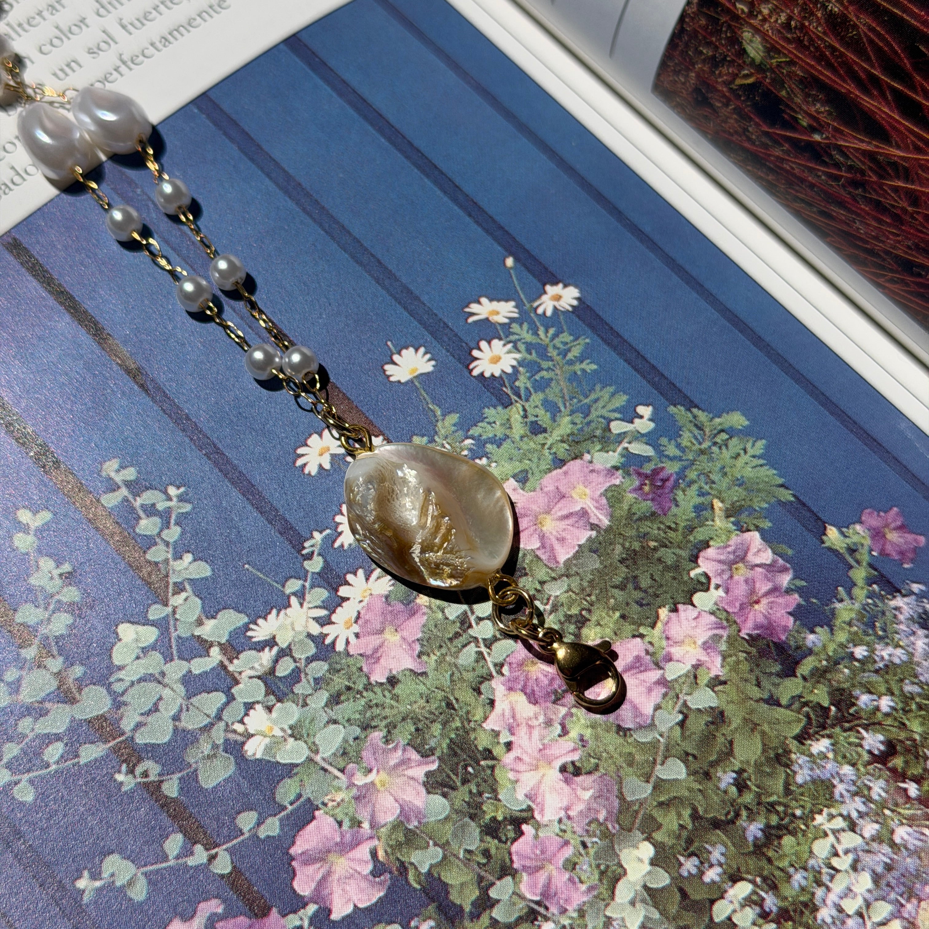Detalle de orquidea marfil encapsulada en resina sobre cadena de perlas y revista botanica