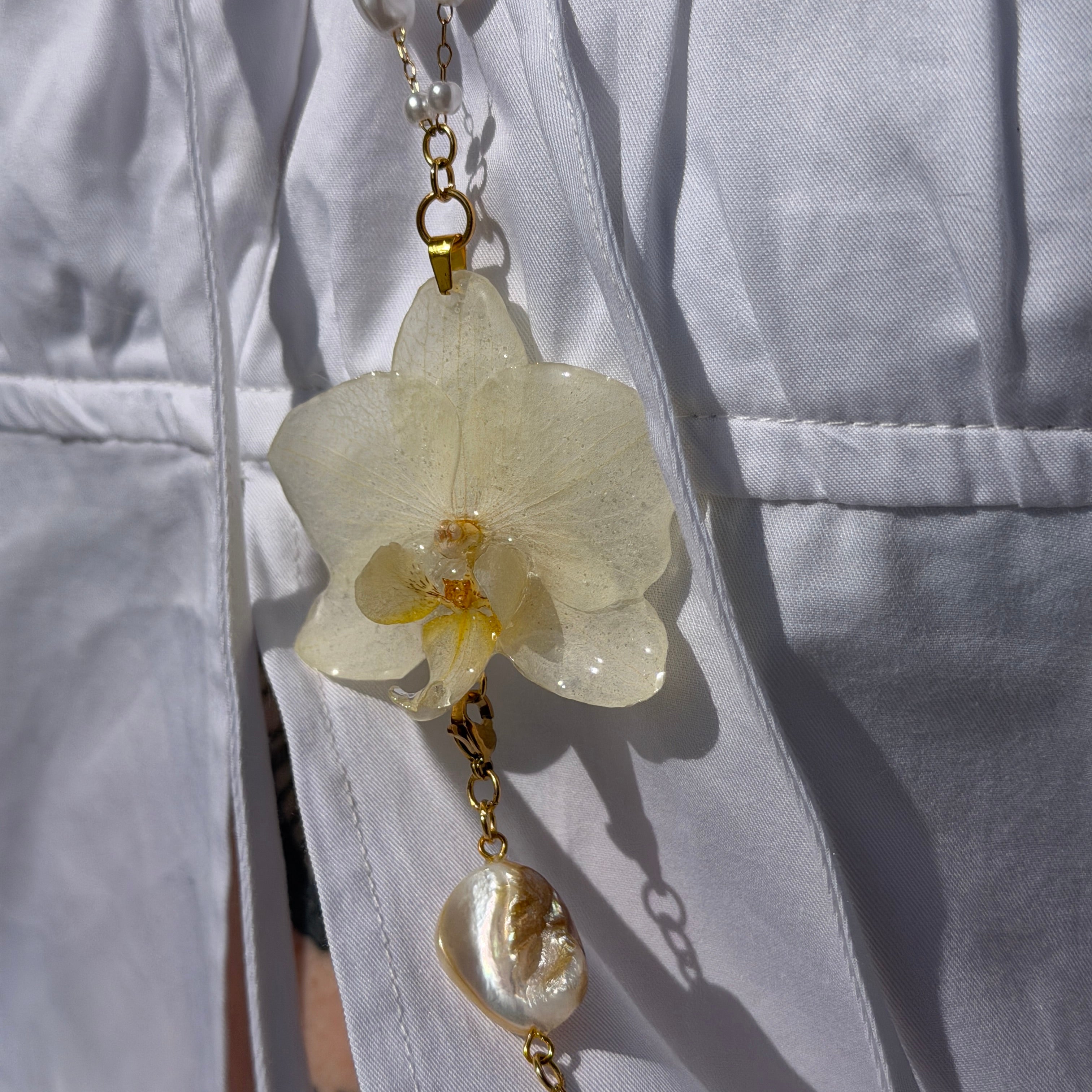 Collar largo con orquidea marfil encapsulada en resina, perlas y perla barroca de agua dulce