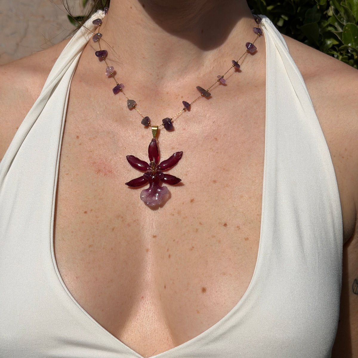 Mujer llevando collar de orquídea Cambria burdeos encapsulada en resina, sobre cadena de amatistas