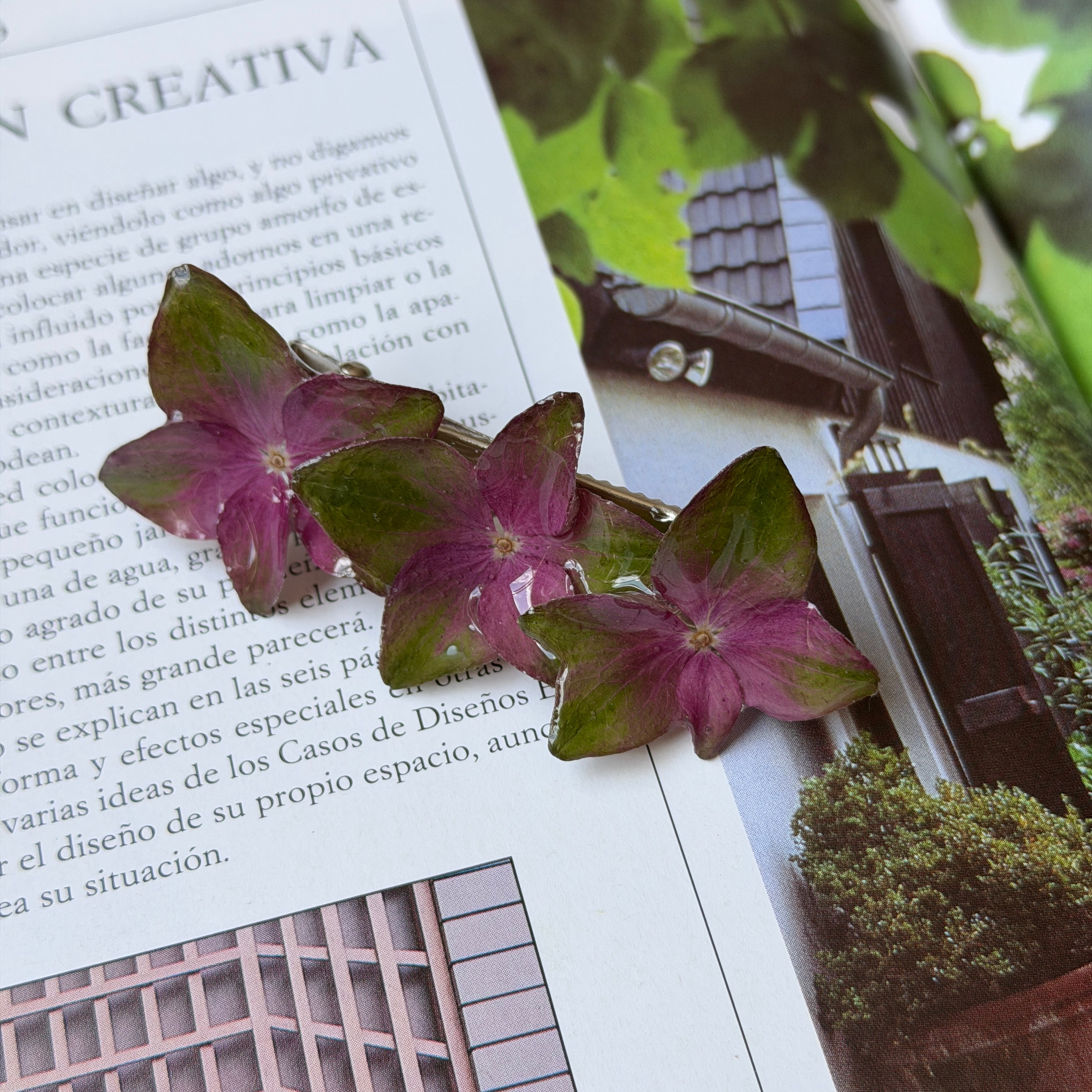 Pinza de tres hortensias fucsia y verde encapsuladas en resina sobre una revista abierta