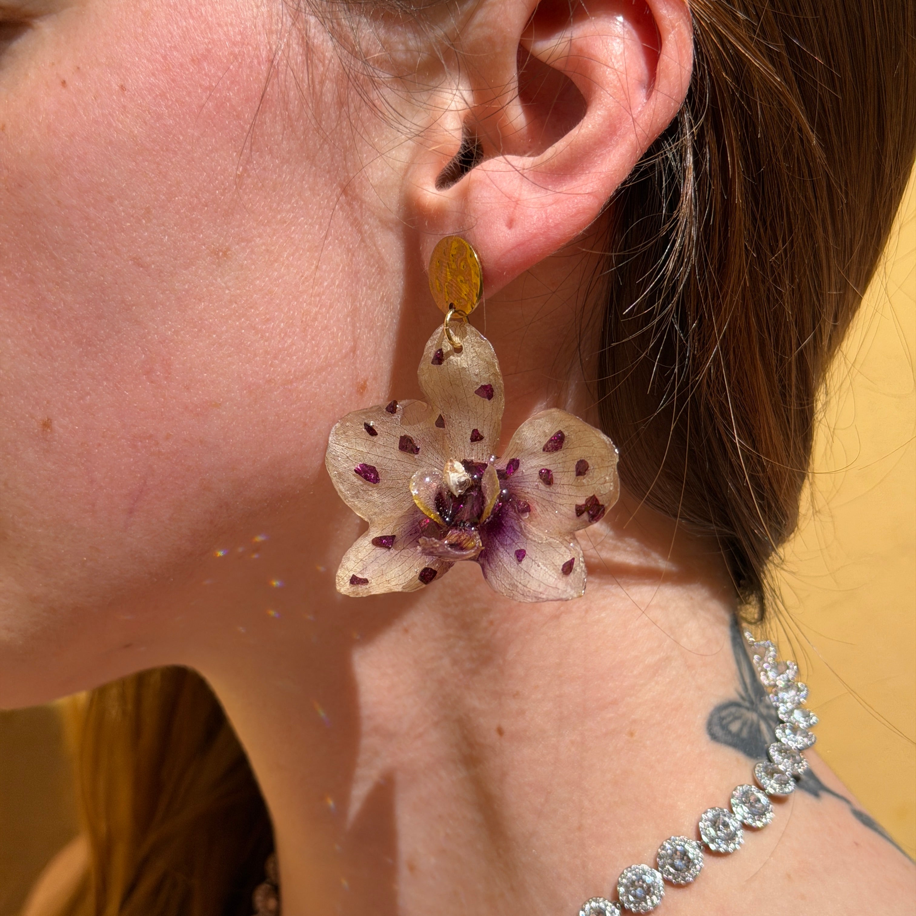 Mujer llevando pendiente de orquídea beige moteada encapsulada en resina sobre la oreja
