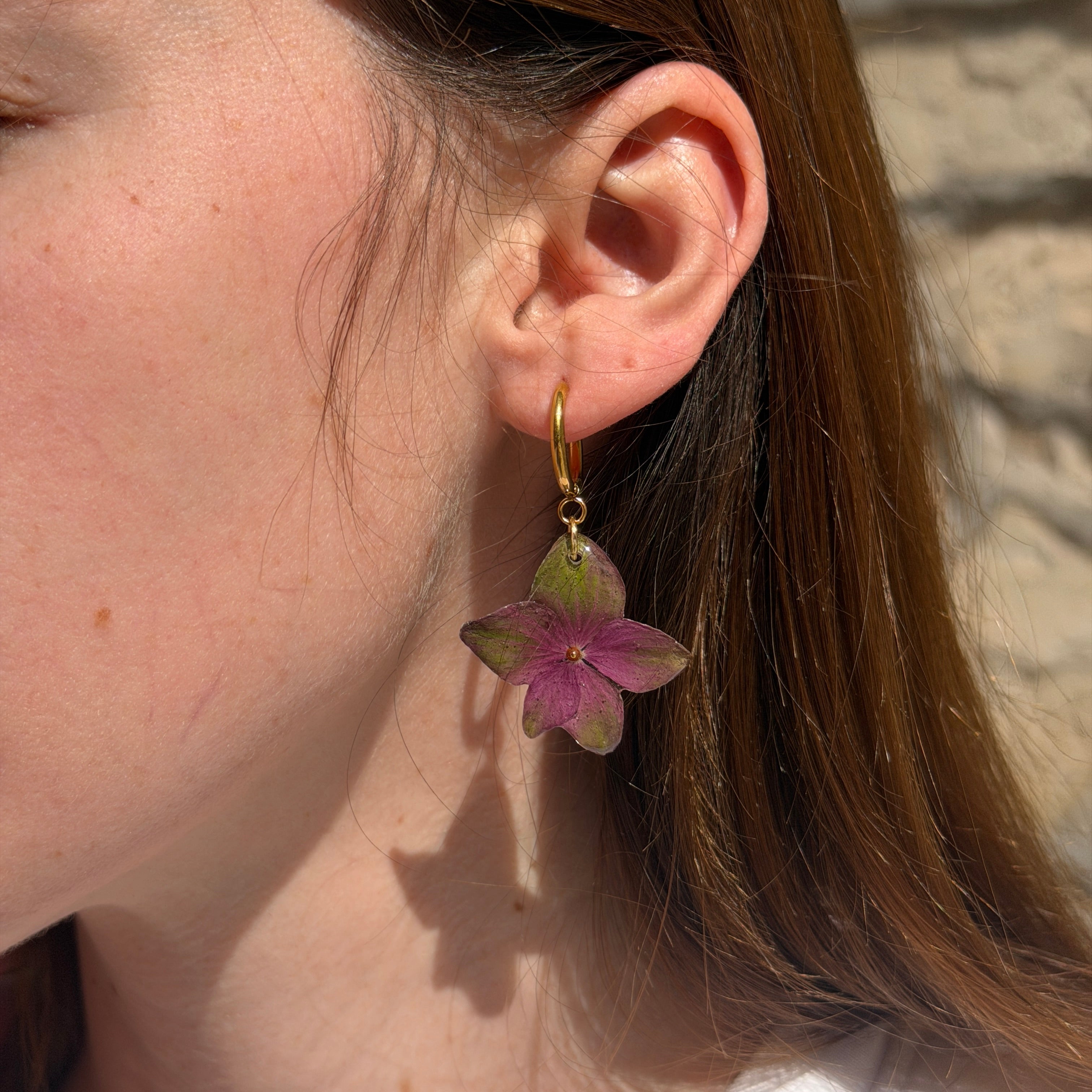 Mujer llevando pendientes de hortensia del fucsia al verde encapsulada en resina sobre la oreja