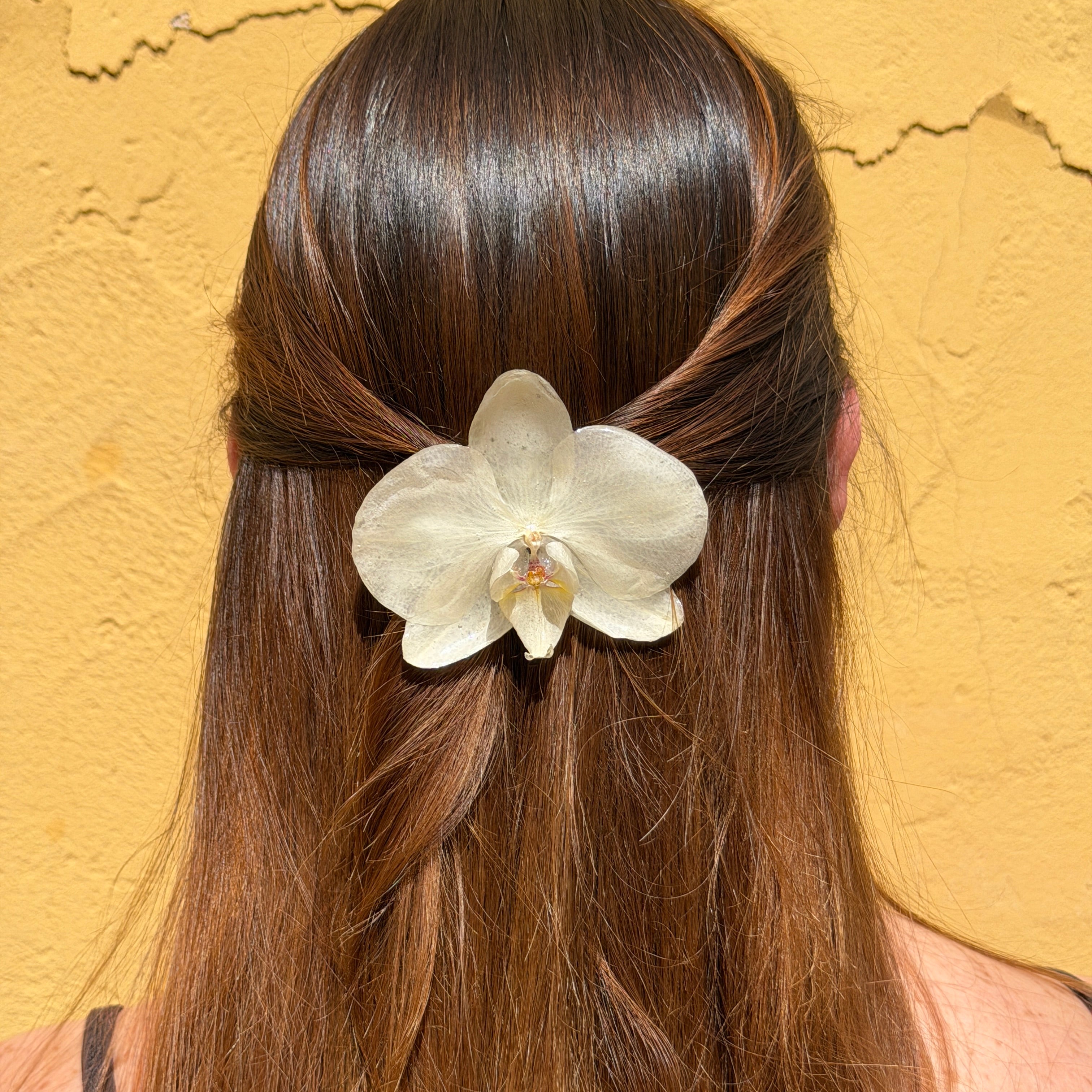 Mujer llevando pinza con orquídea marfil encapsulada en resina sobre el pelo
