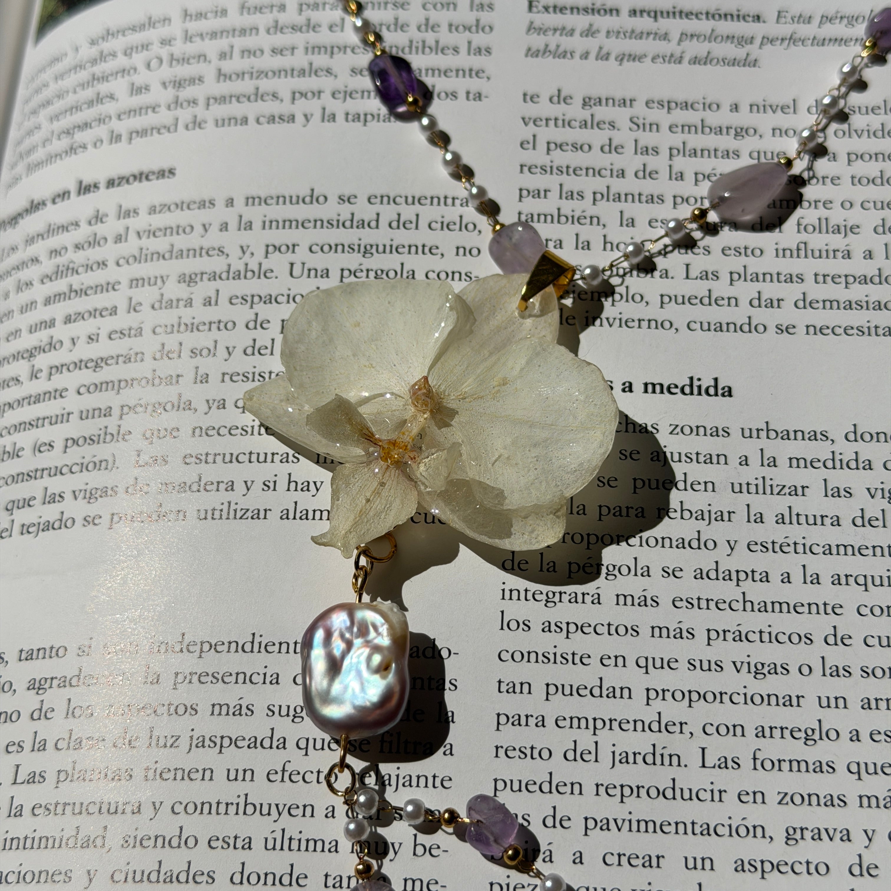 Collar de orquídea blanca encapsulada en resina con perla barroca, sobre las páginas de un libro