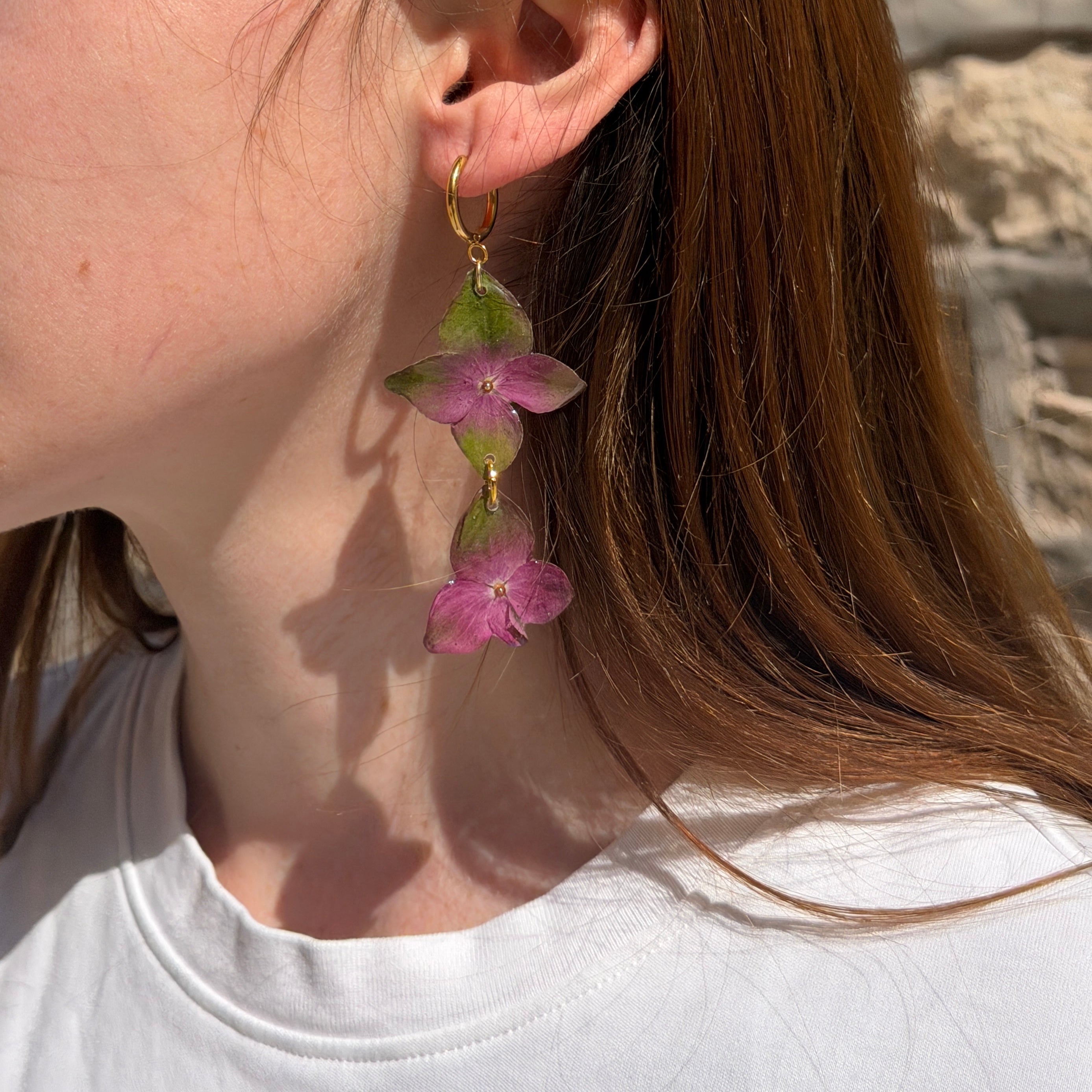 Mujer llevando pendiente de hortensia verde y fucsia encapsulada en resina sobre la oreja