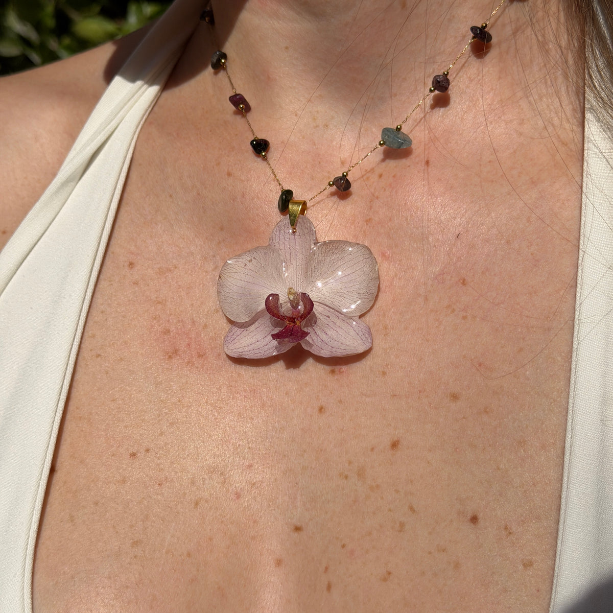 Mujer llevando collar de orquídea blanca encapsulada en resina, sobre cadena de piedras naturales