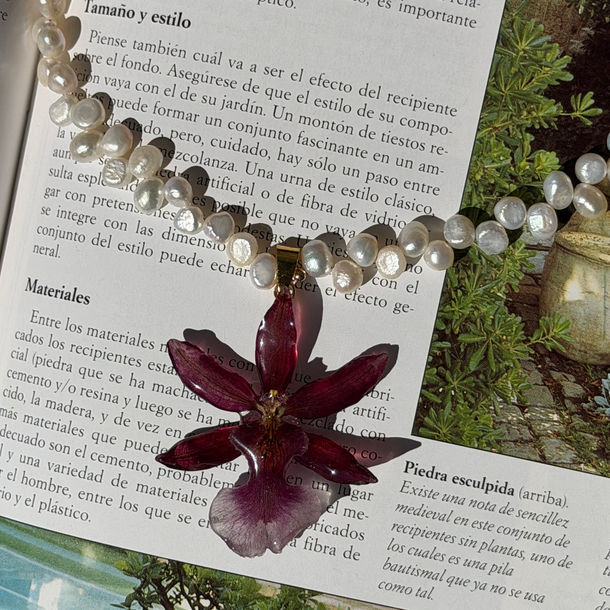 Collar de orquídea Cambria burdeos encapsulada en resina con cadena de perlas, sobre un libro abierto